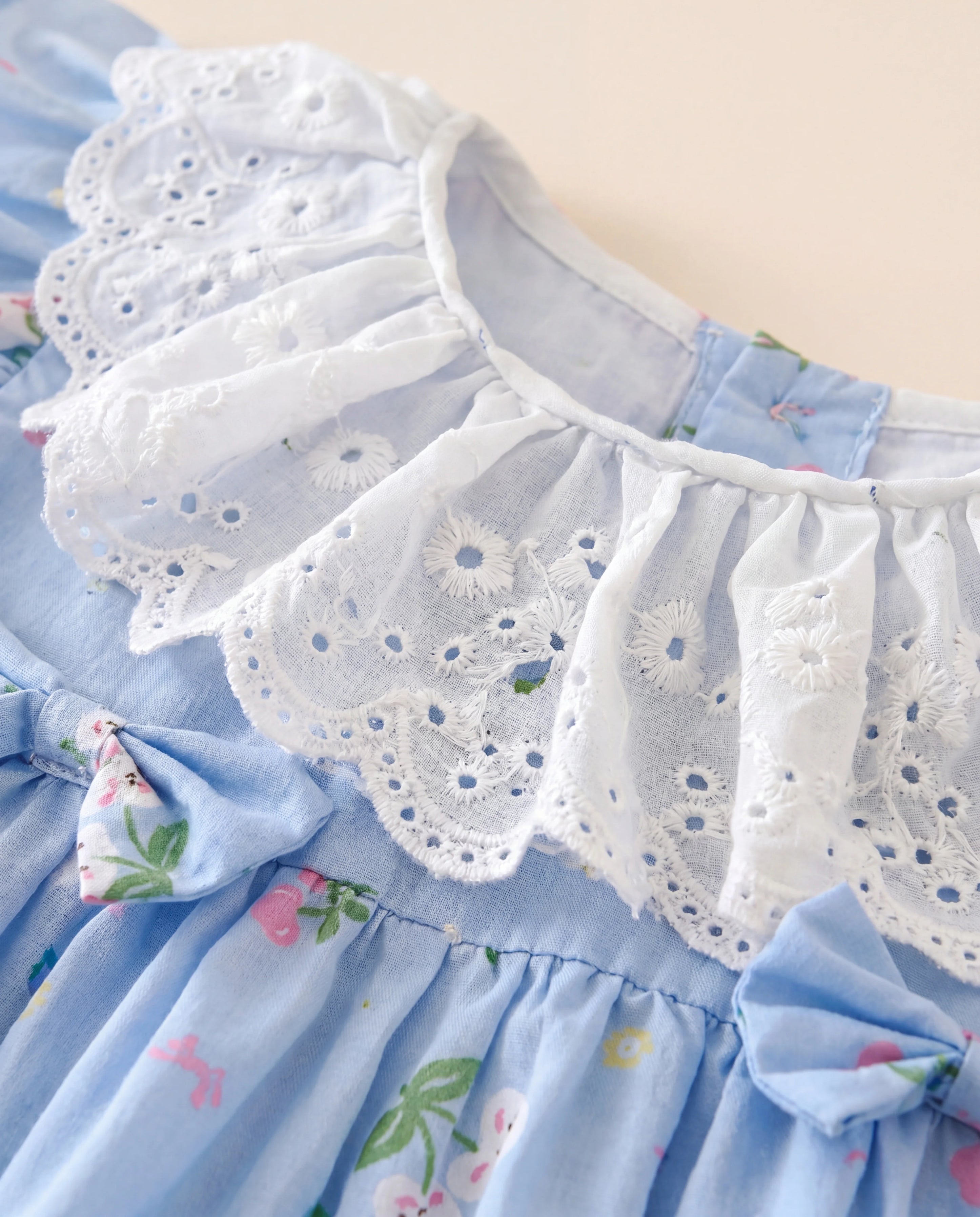 Close-up of a blue dress with floral patterns and white lace trim on a beige background