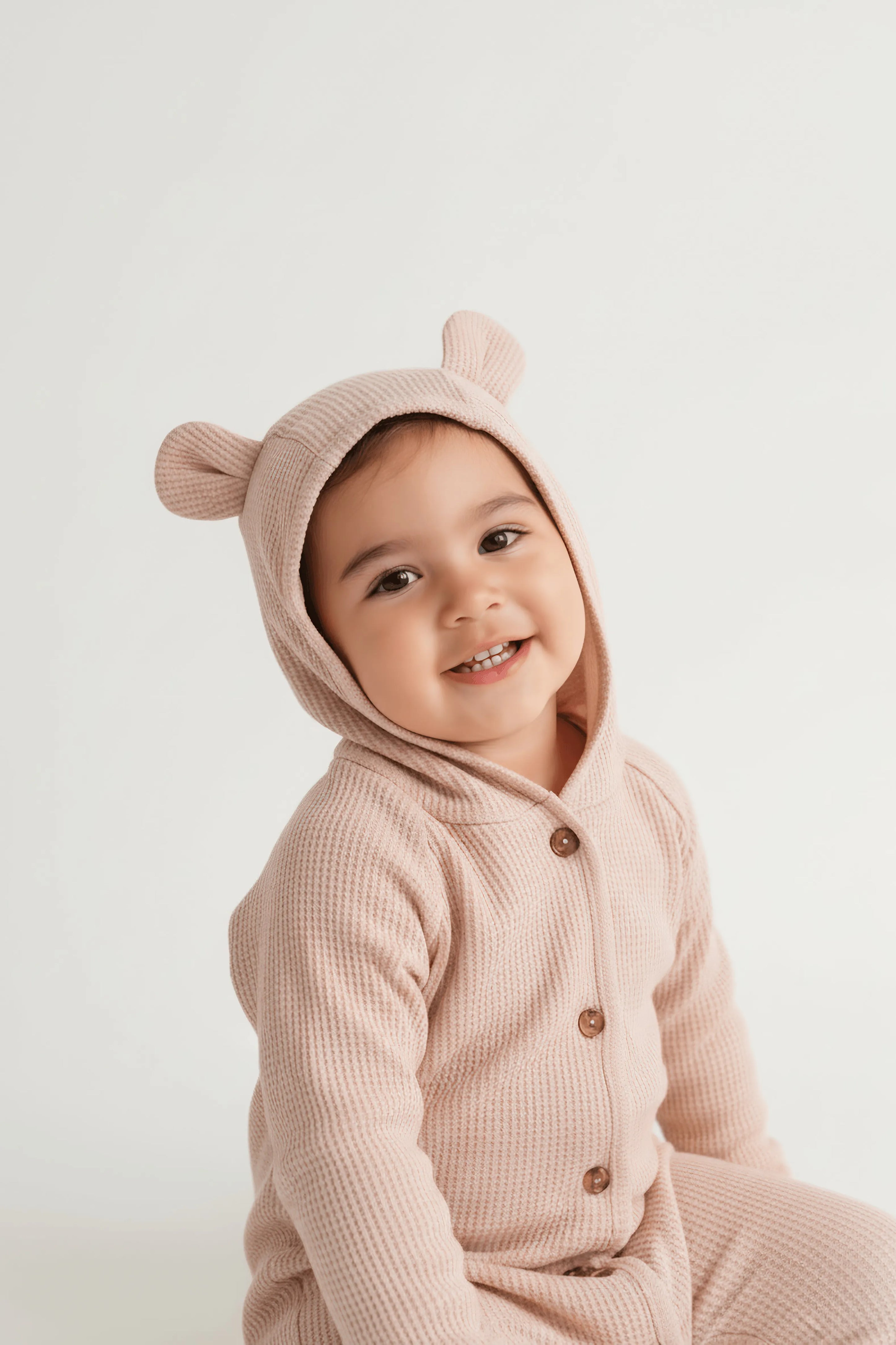 Child wearing a pink bear-themed Bubba's and Mama's onesie with a hood on a white background