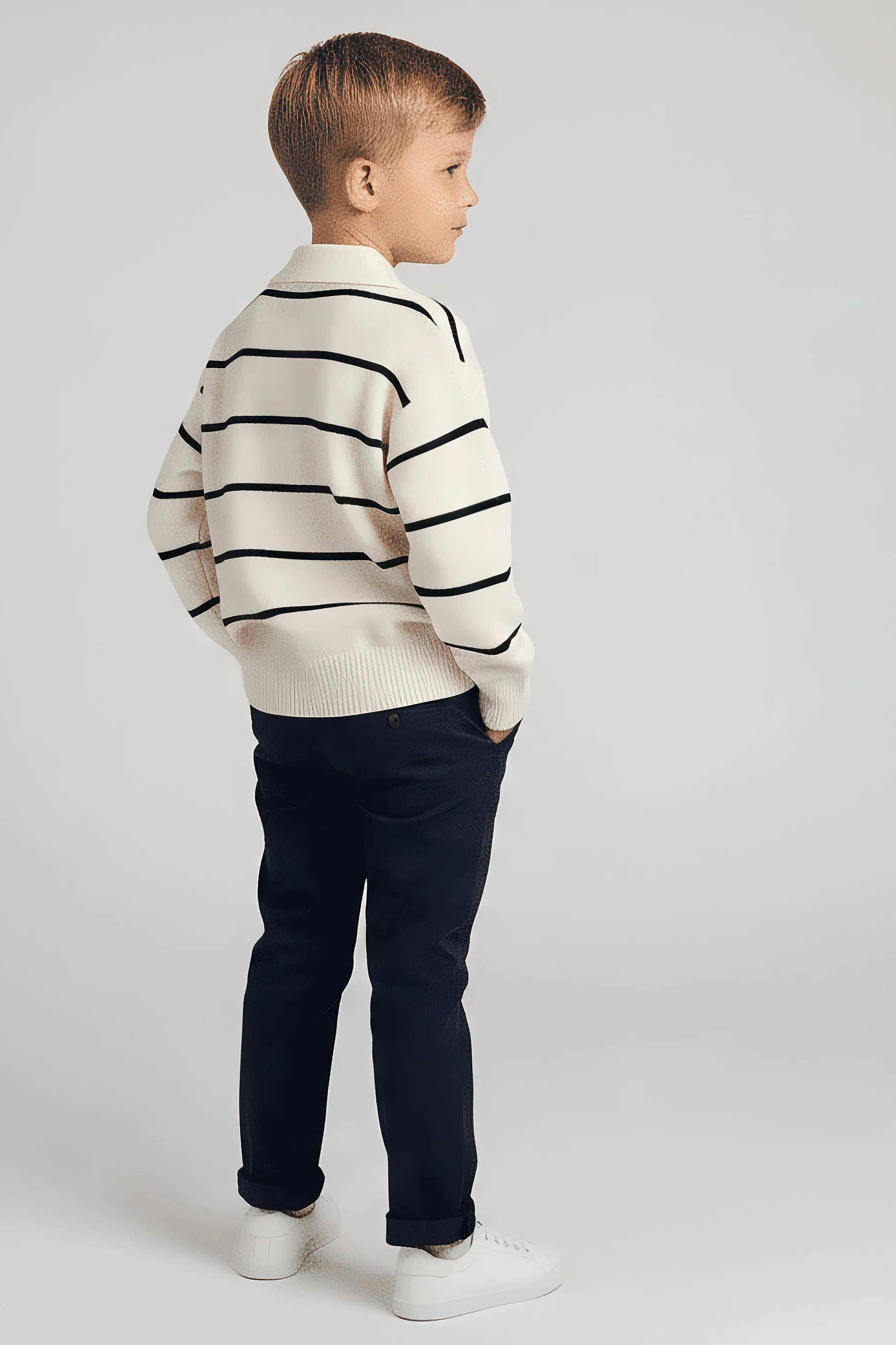 Child wearing a striped Bubba's and Mama's sweater and navy pants on a light gray background