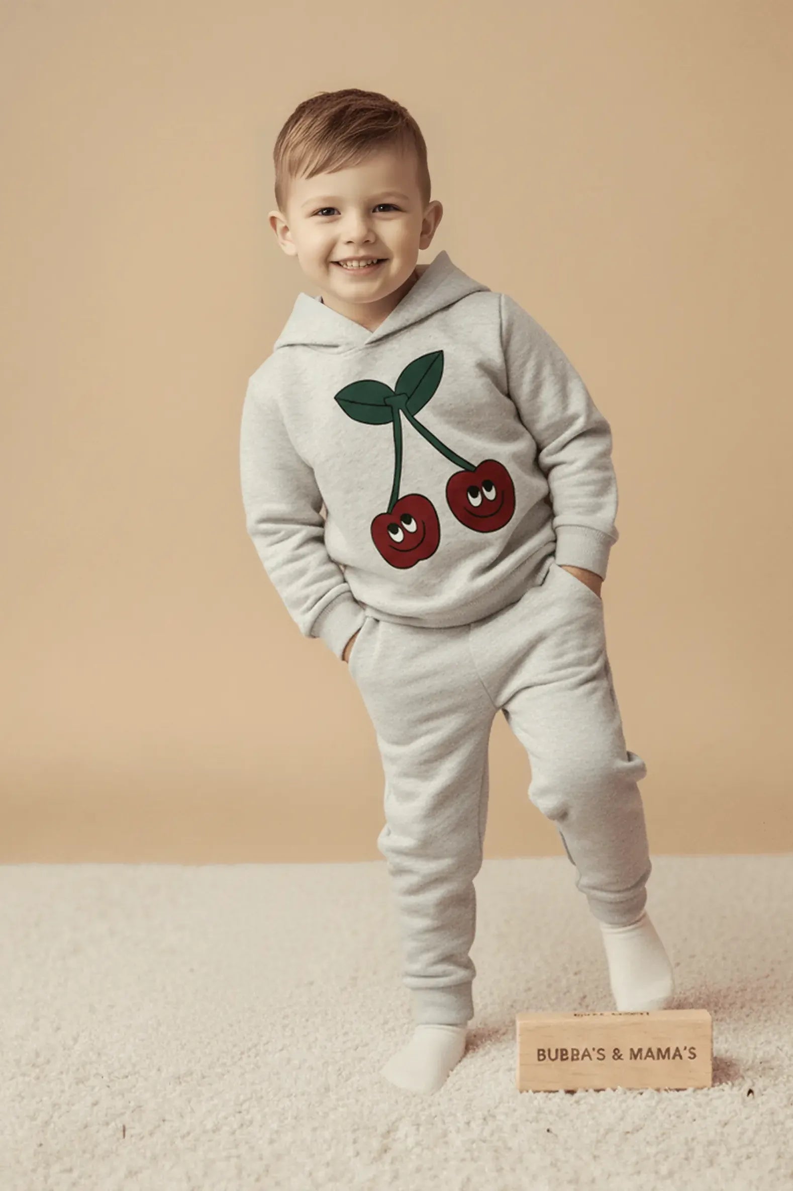 Child wearing a gray Bubba's and Mama's hoodie and pants with cherry design on a beige background