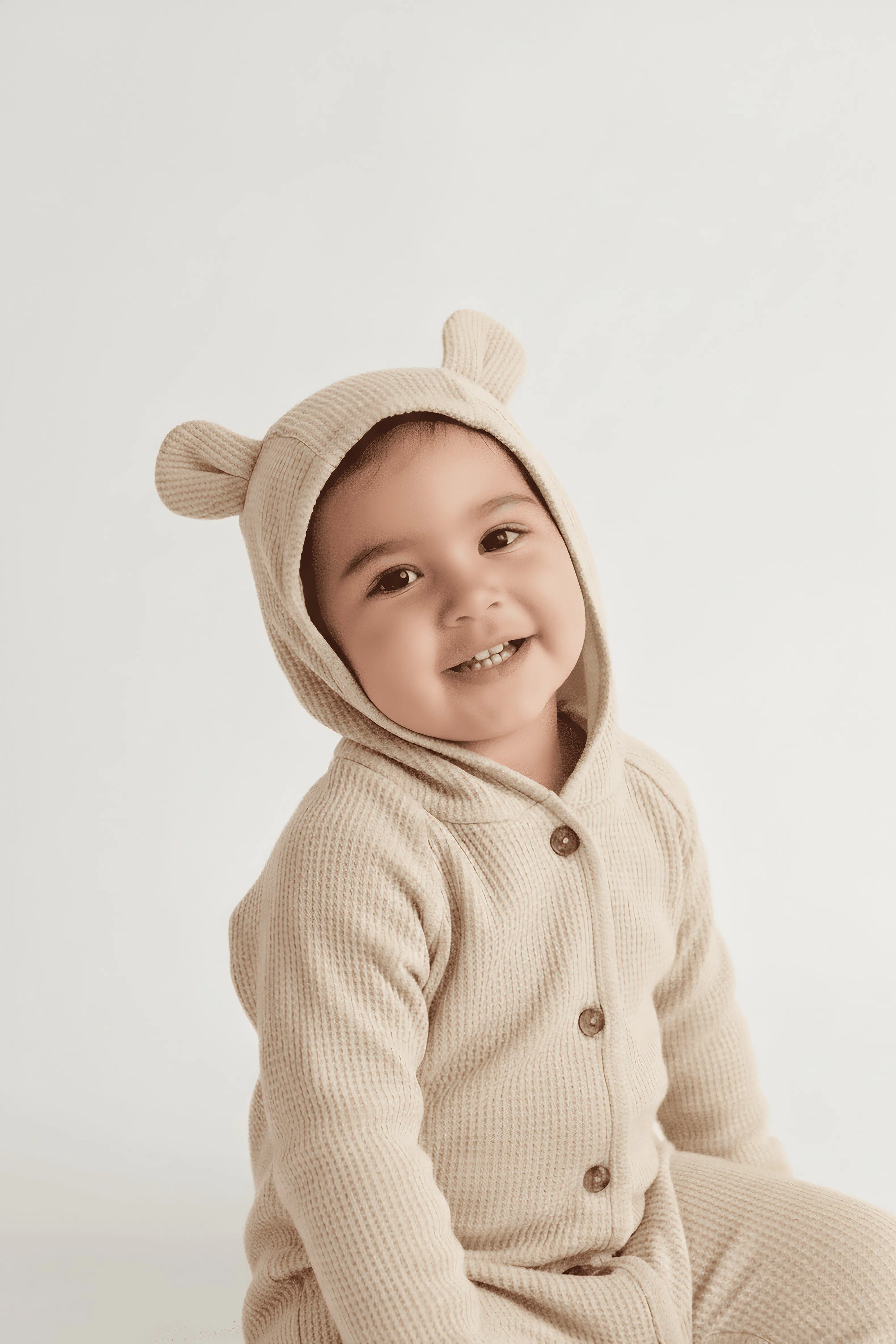 Child wearing a beige bear-themed Bubba's and Mama's onesie with a hood on a white background