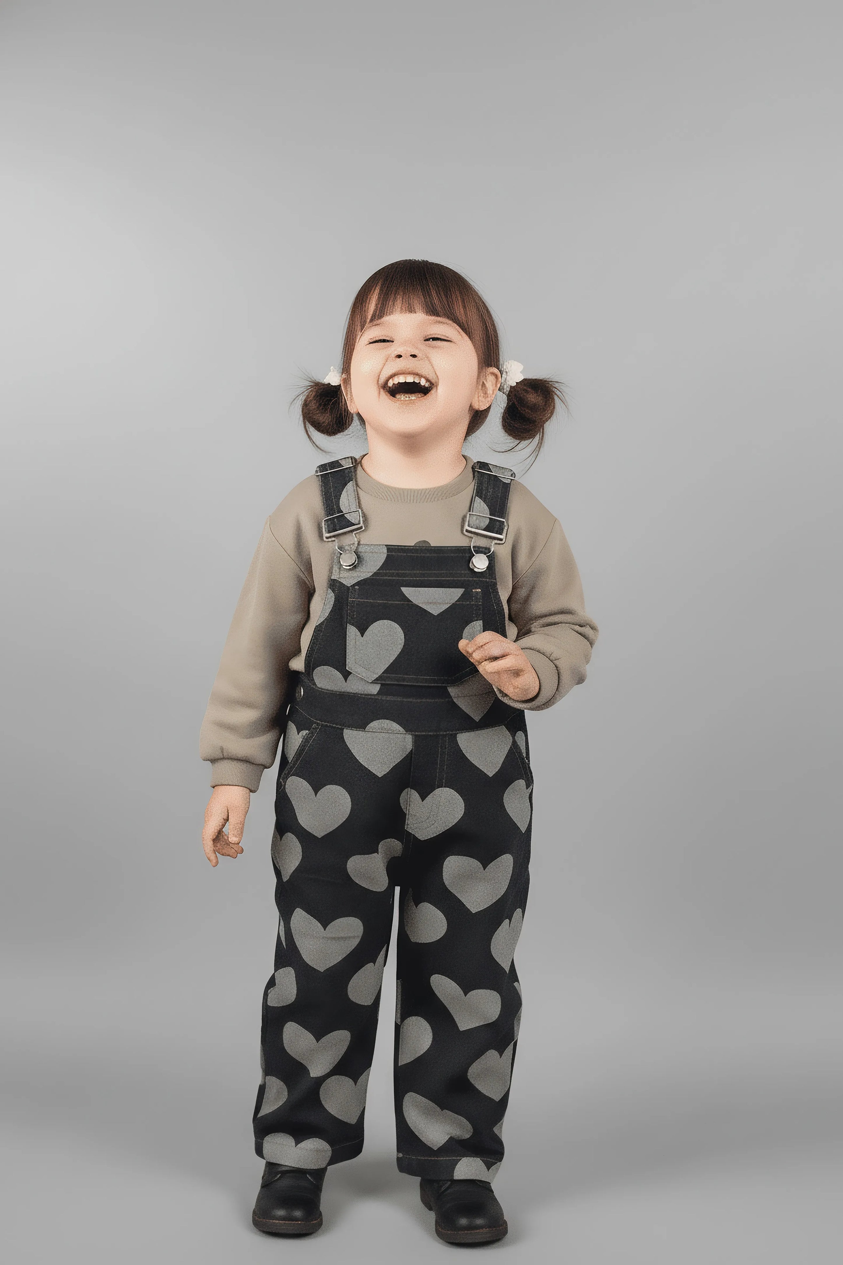 Child wearing heart-patterned Bubba's and Mama's overalls on a gray background