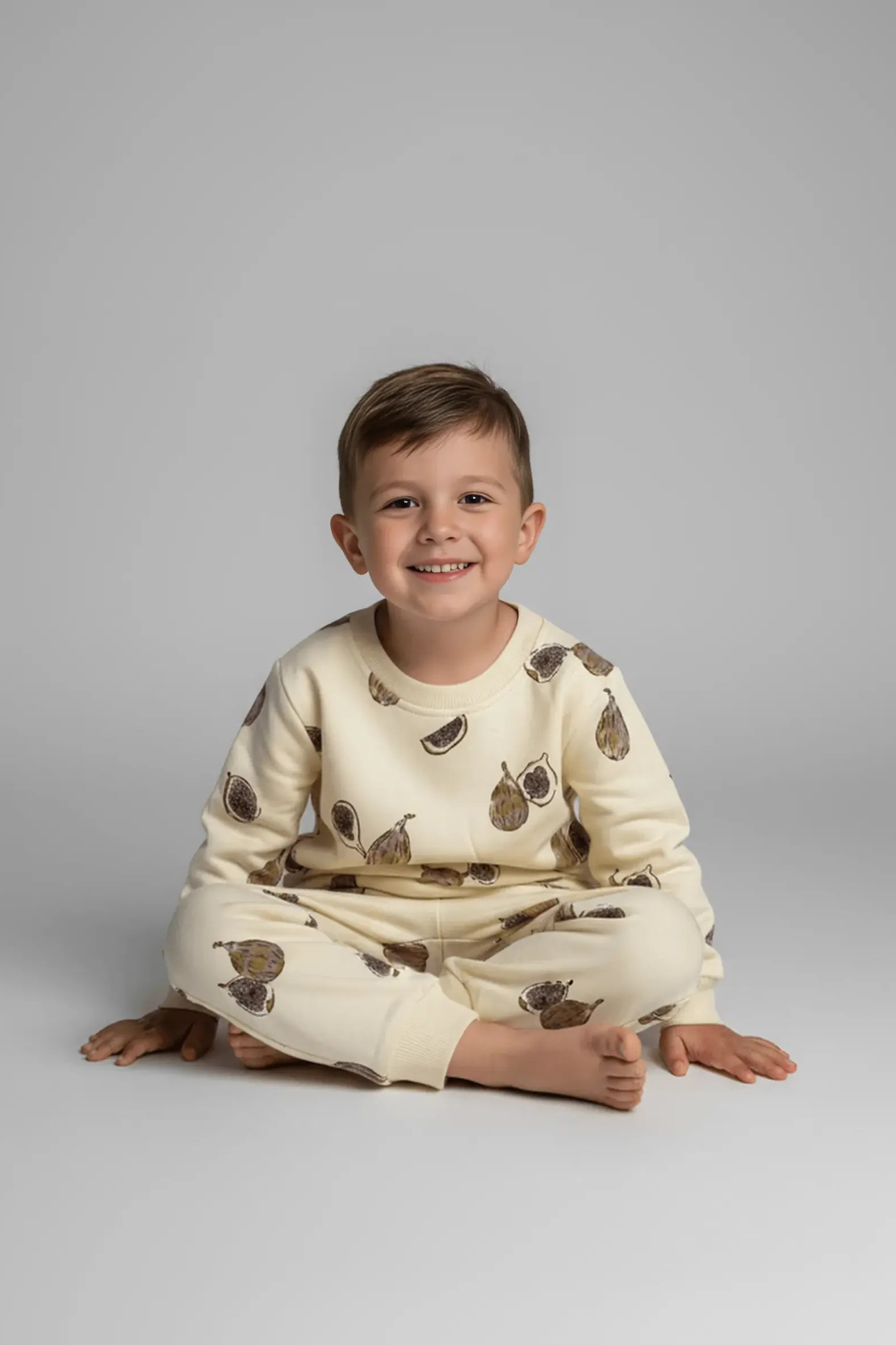 Child wearing a cream-colored Bubba's and Mama's outfit with brown fig prints on a gray background
