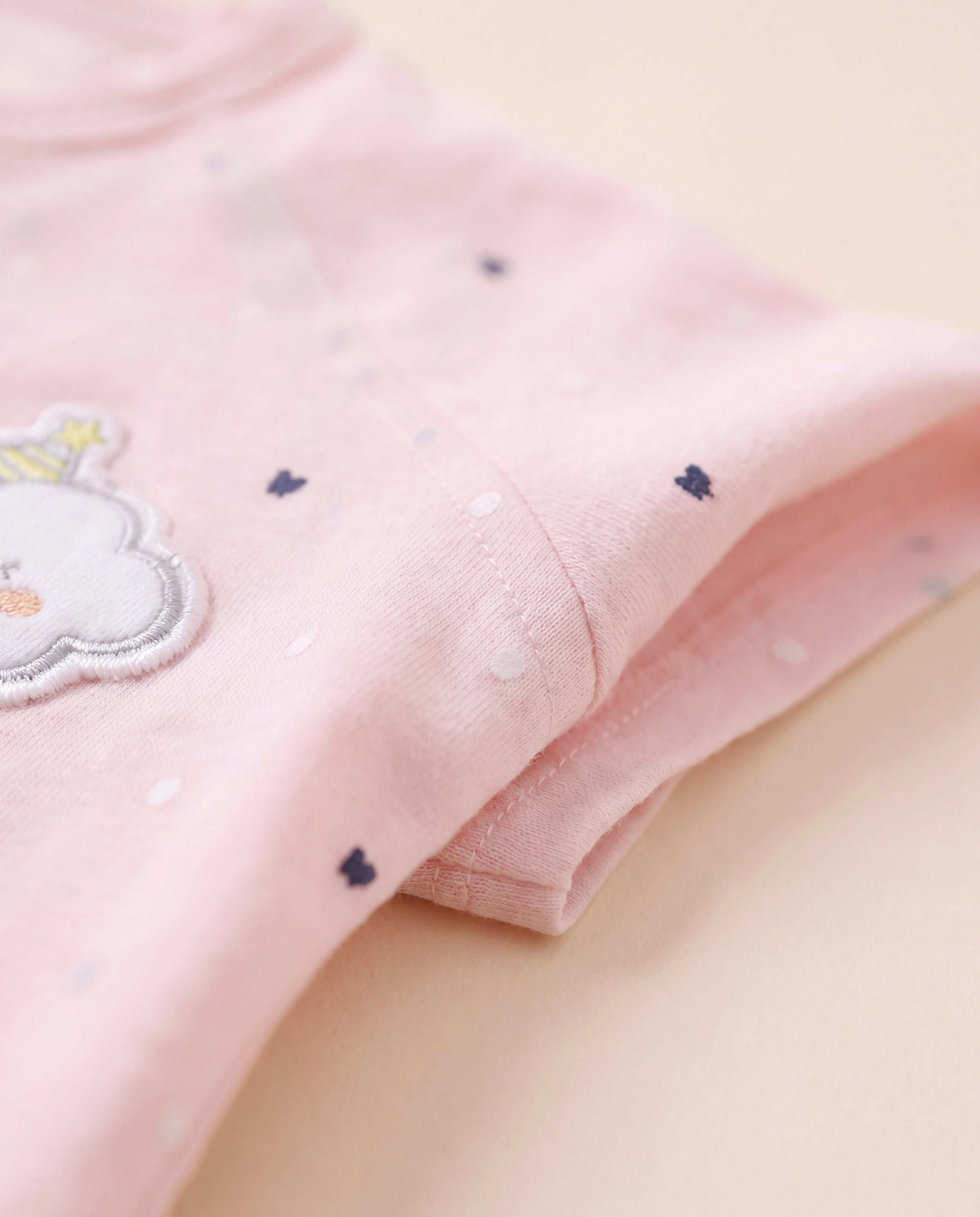 Close-up of pink fabric with embroidered cloud design on a light yellow background