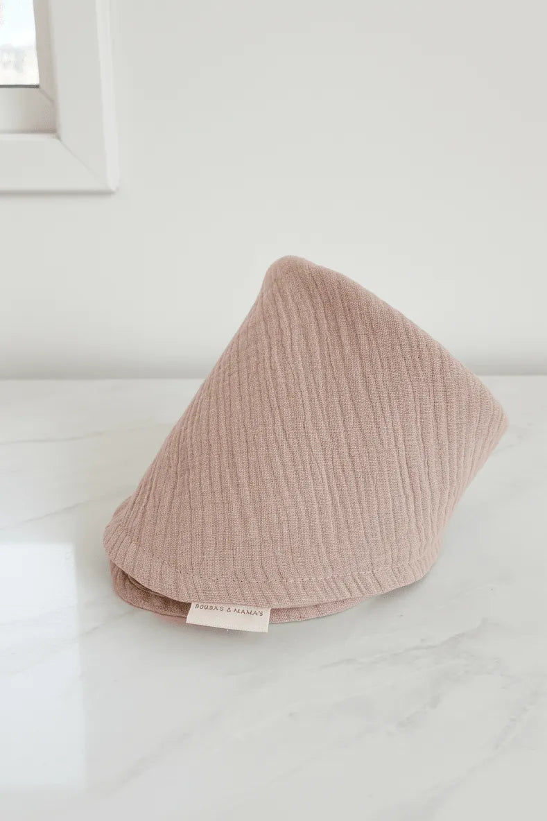 Pink textured Lux Muslin Baby Bib on a white surface with a blurred background.