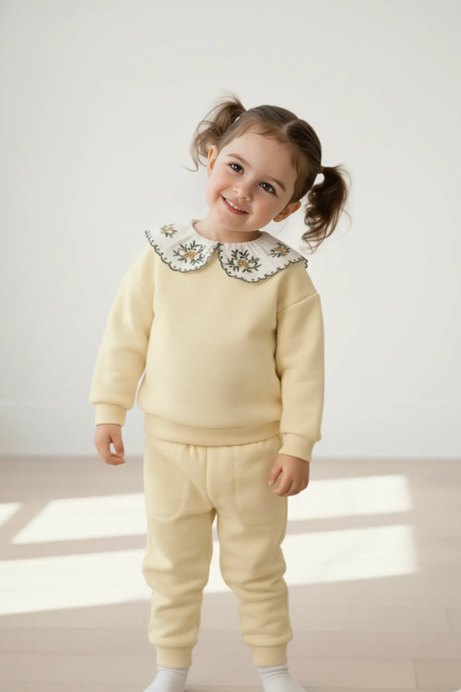 Child wearing a light yellow Bubba's and Mama's outfit with a floral collar on a neutral background