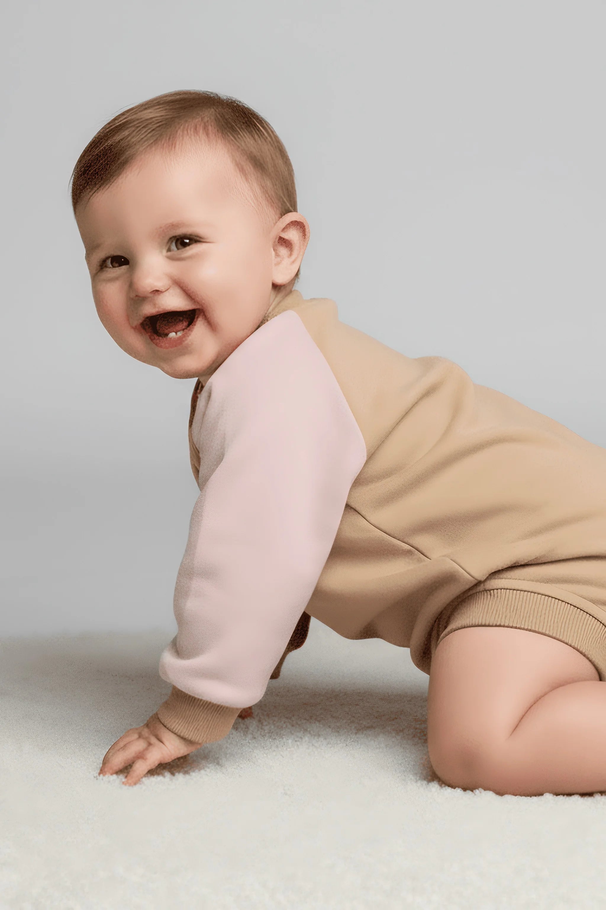 Baby in a pink and beige Bubba's and Mama's outfit crawling on a light gray background