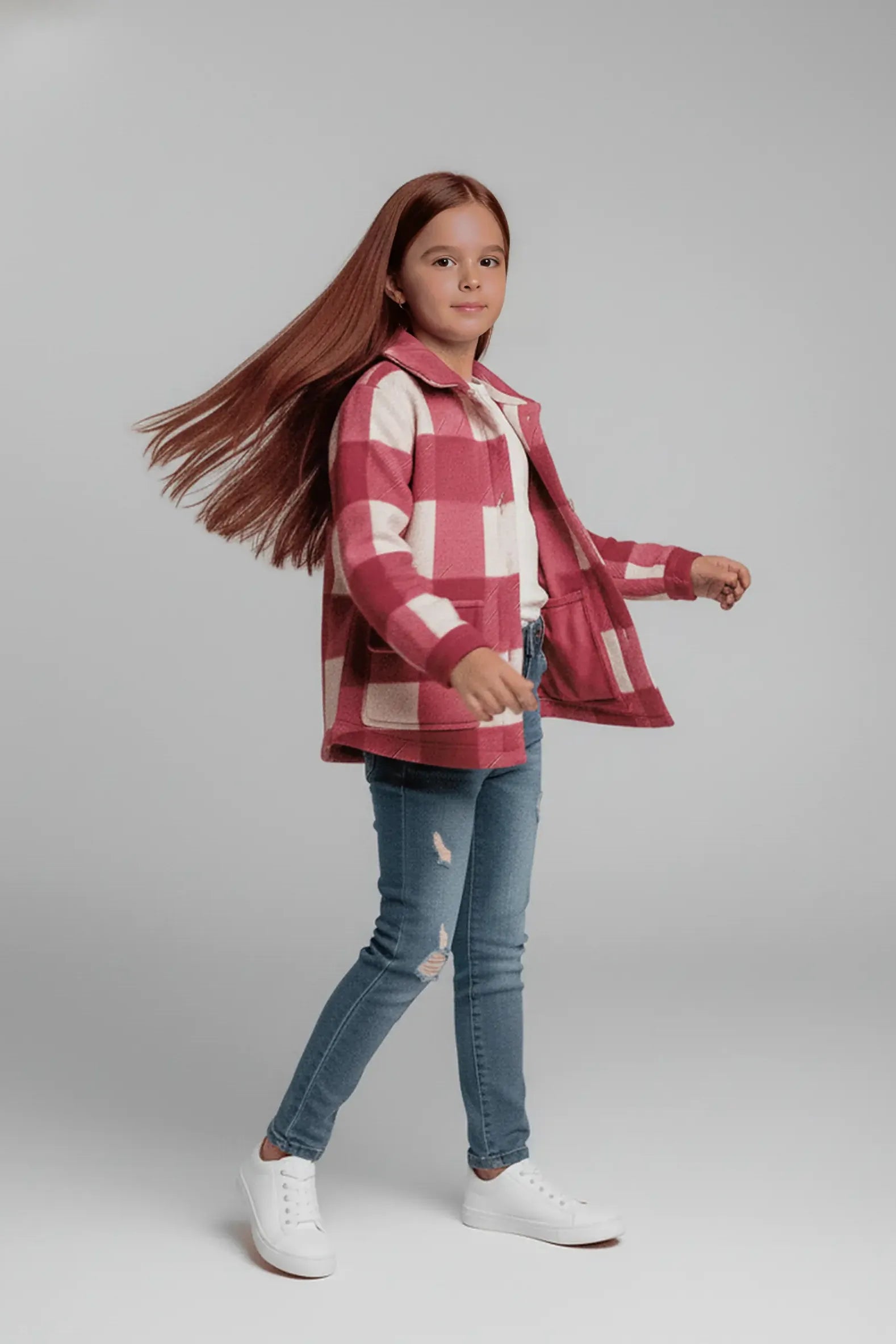 Young girl wearing a red and white checkered Bubba's and Mama's jacket with blue jeans on a gray background