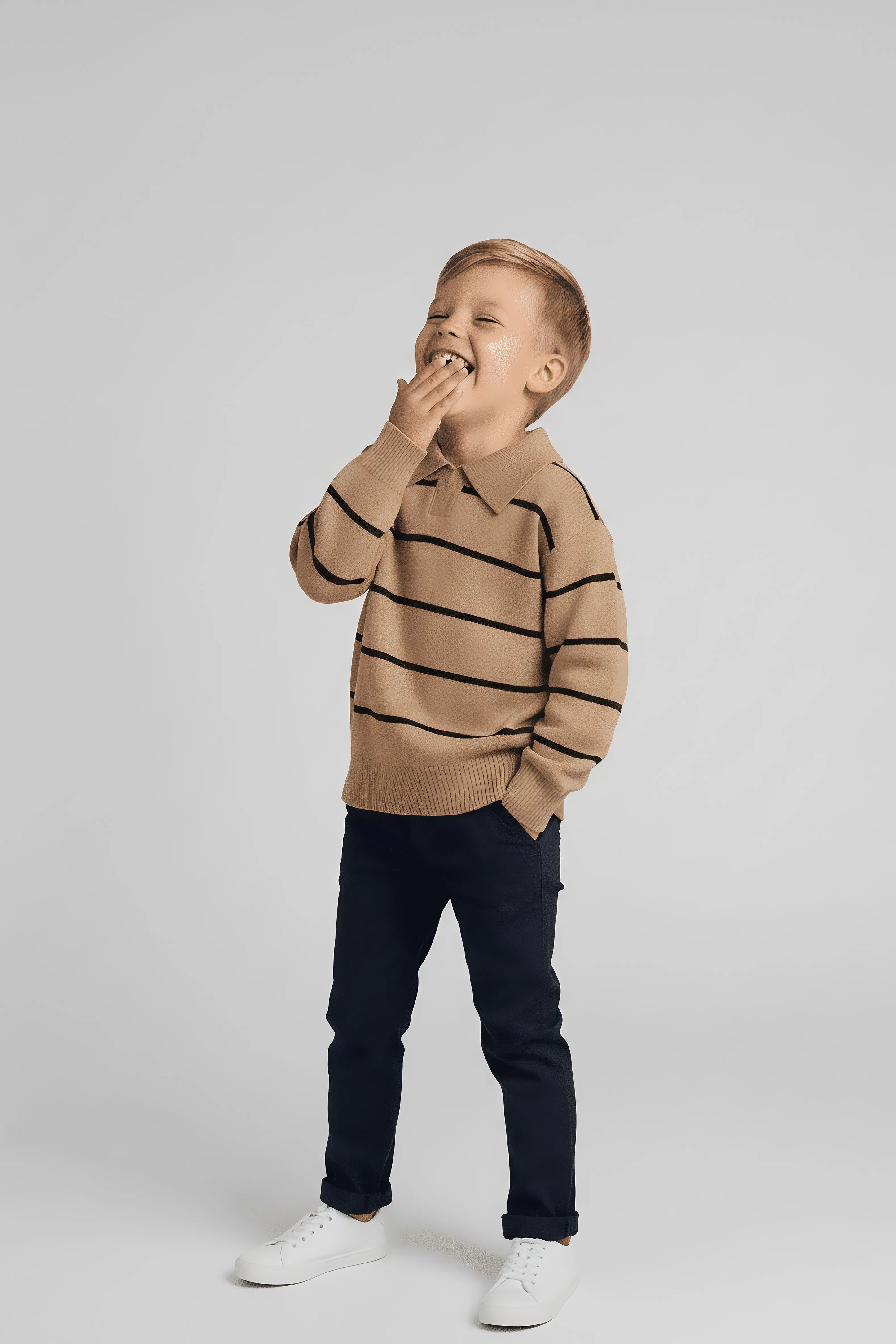 Child wearing a brown Bubba's and Mama's striped sweater and dark pants on a light gray background