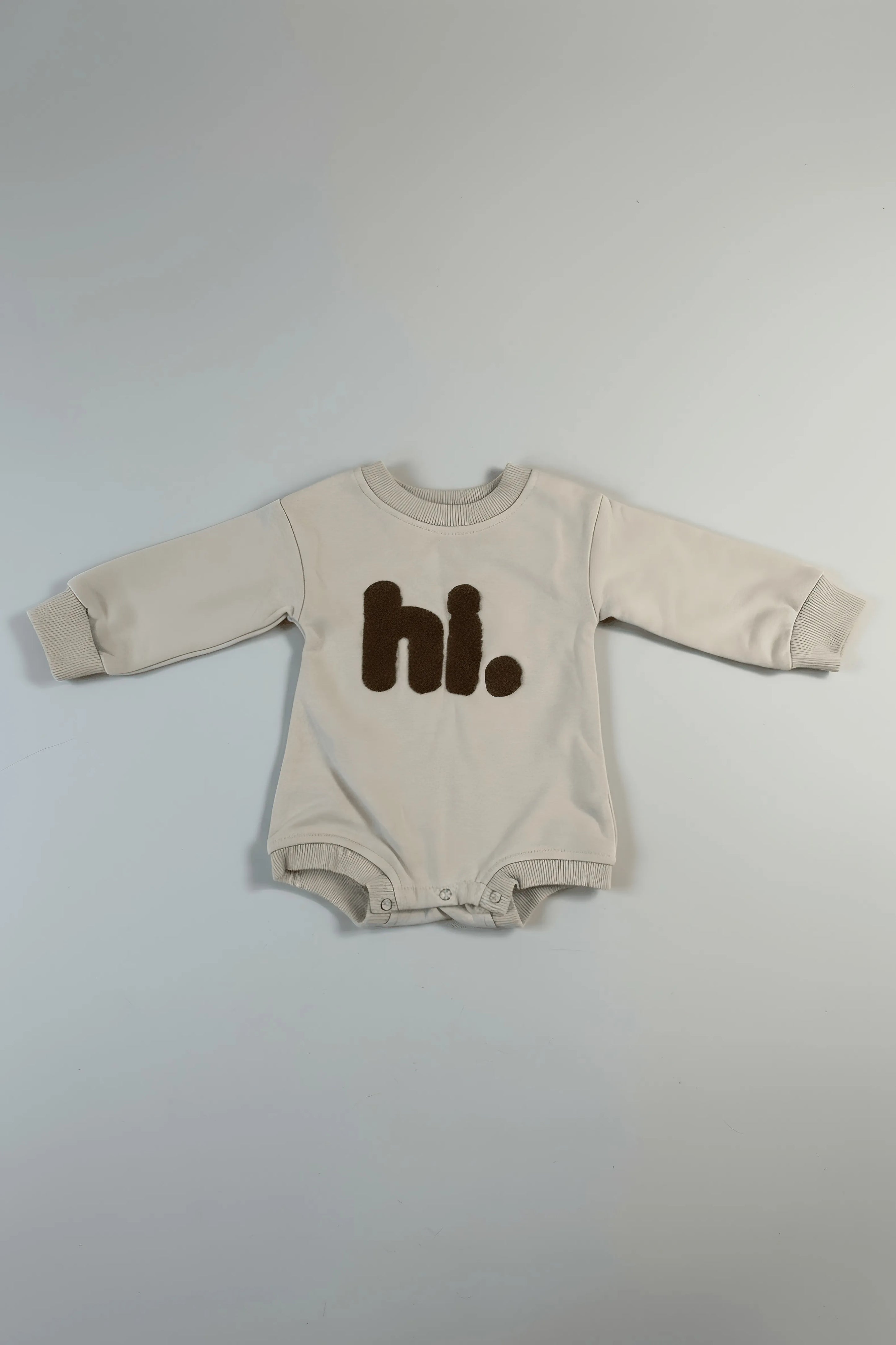 Beige baby Bubba's and Mama's onesie with 'hi.' text on a gray background