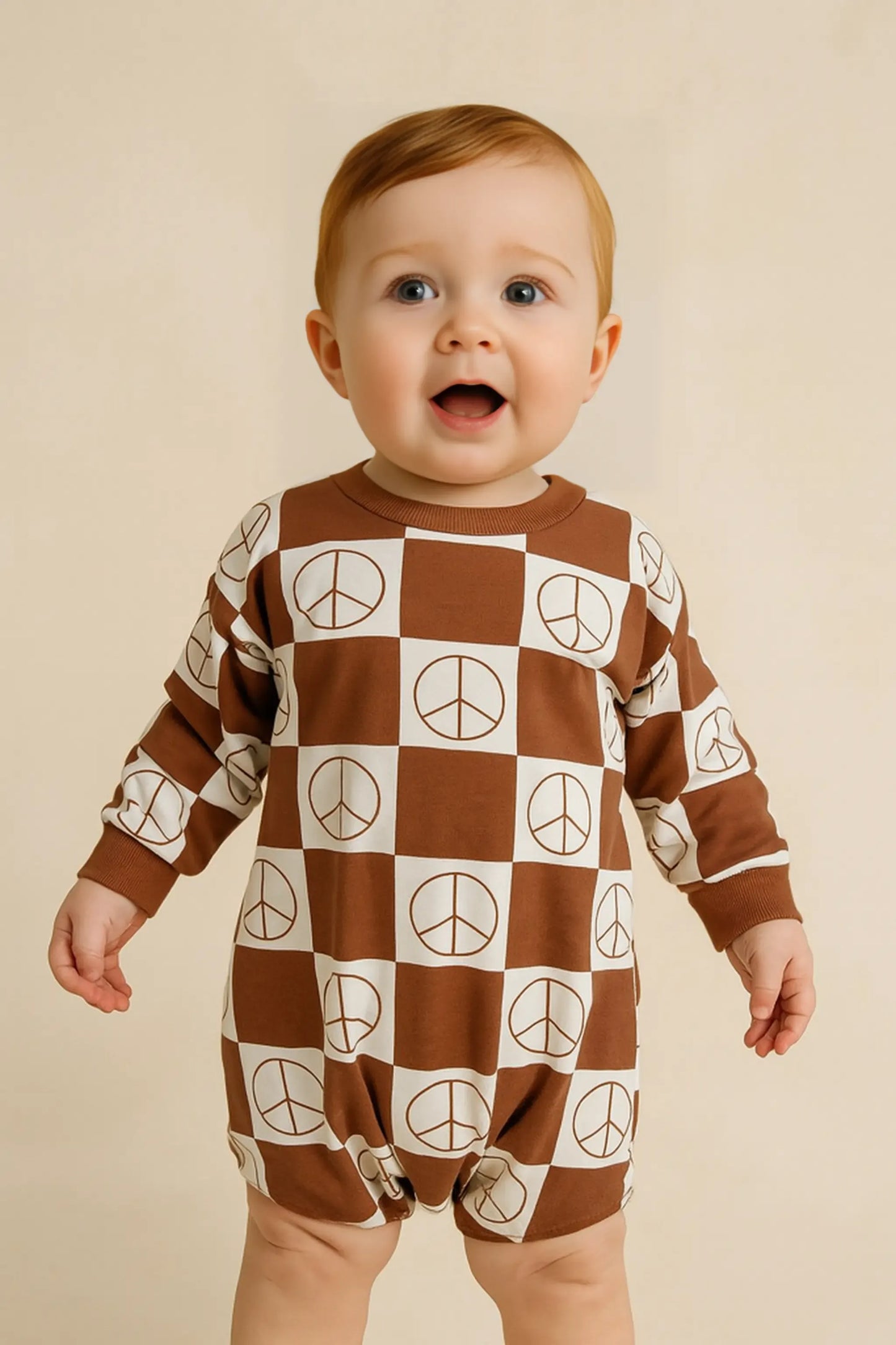 Baby wearing a brown and white checkered onesie with peace signs on a beige background