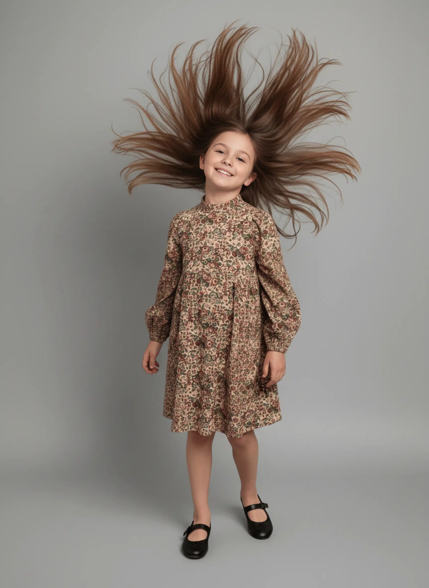 Young girl with long brown hair styled upwards wearing a floral dress on a gray background
