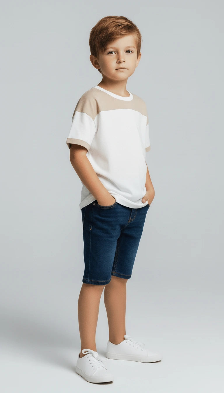 Young boy wearing a white and beige shirt with blue shorts on a light gray background