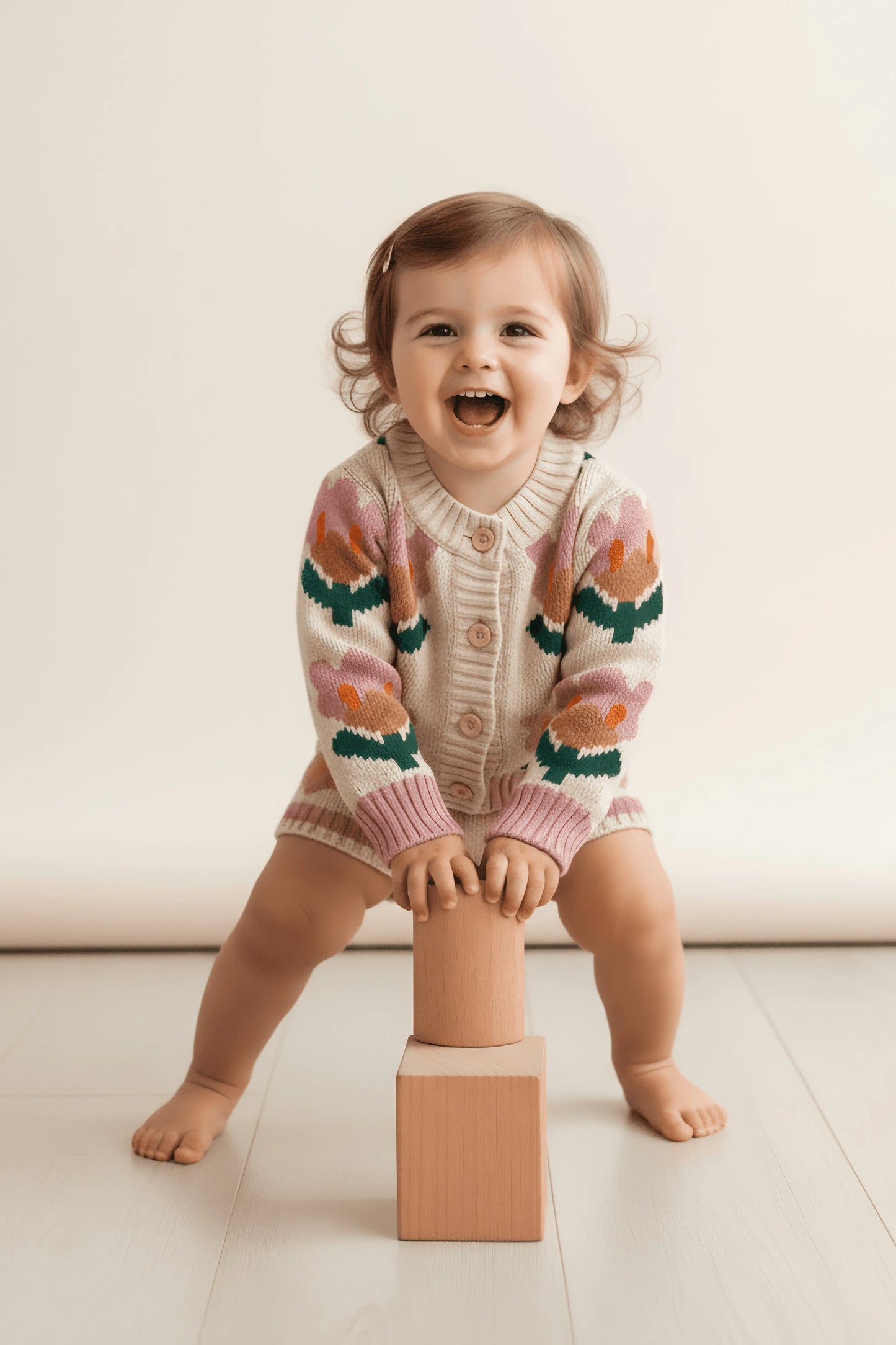 Child wearing a colorful Bubba's and Mama's sweater sitting on a wooden block against a plain background