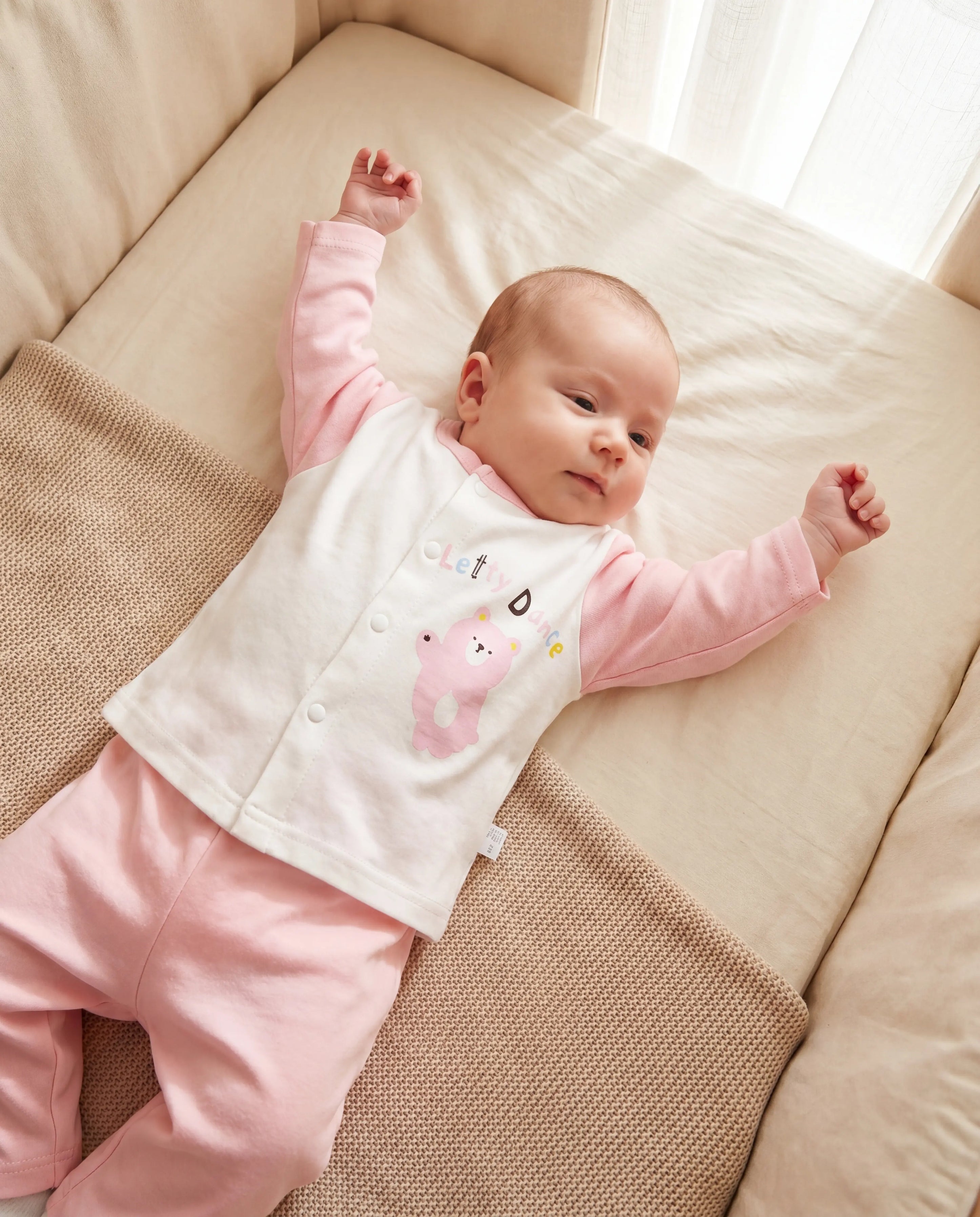 Baby in pink outfit lying on a beige couch