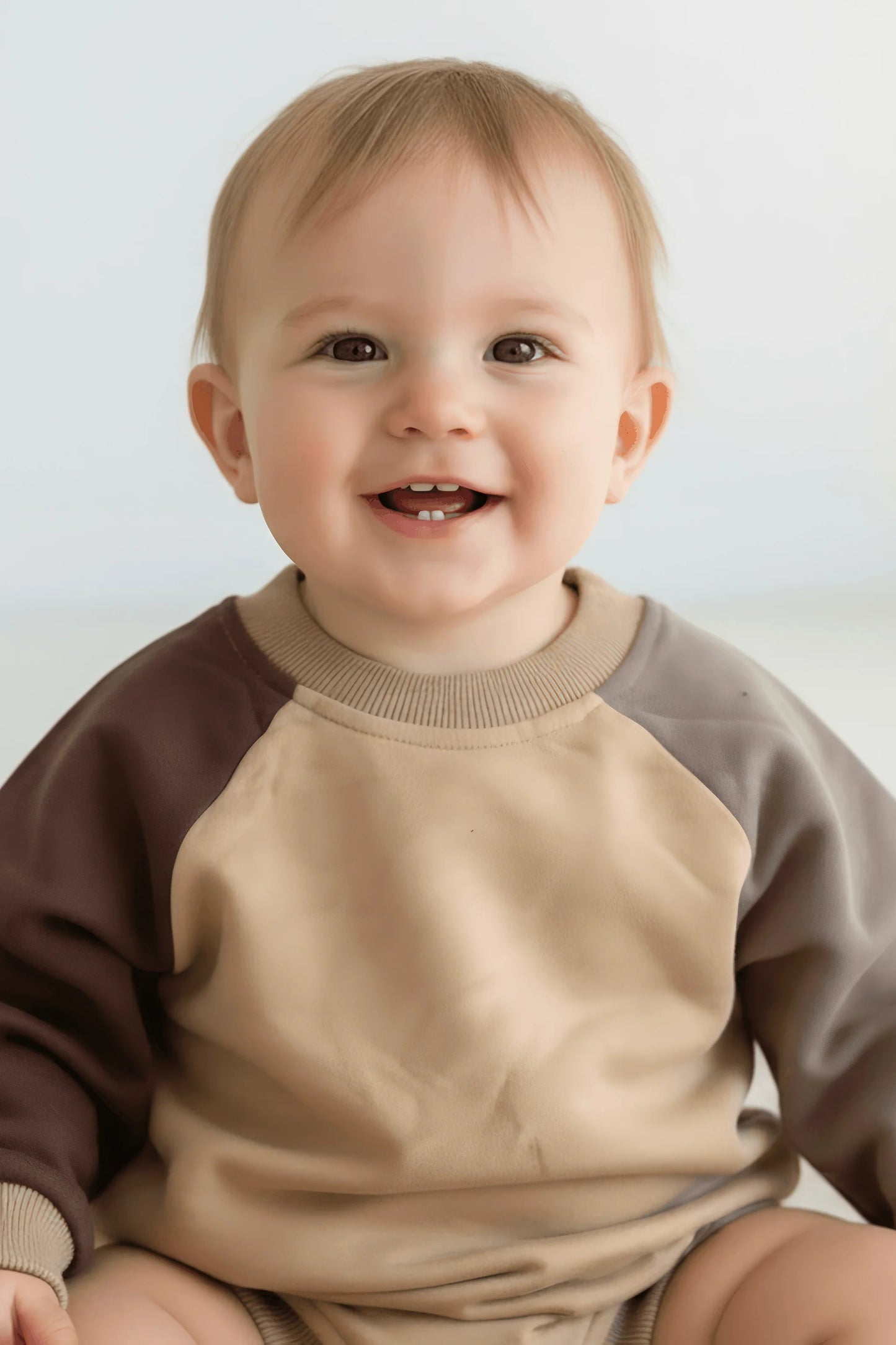 Child wearing a two-tone brown and beige Bubba's and Mama's romper against a plain background