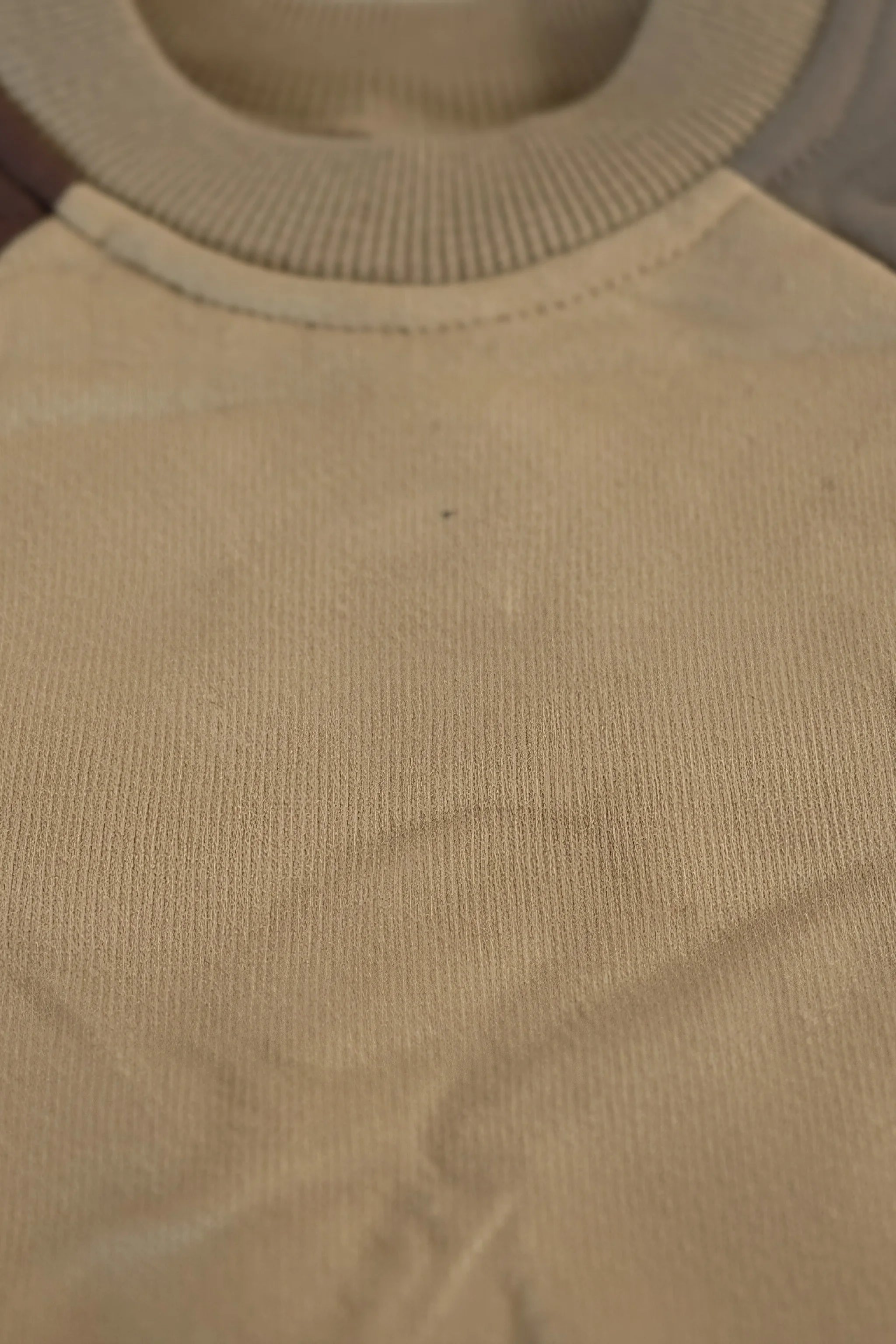 Close-up of a beige Bubba's and Mama's romper with visible fabric texture and a small black speck.