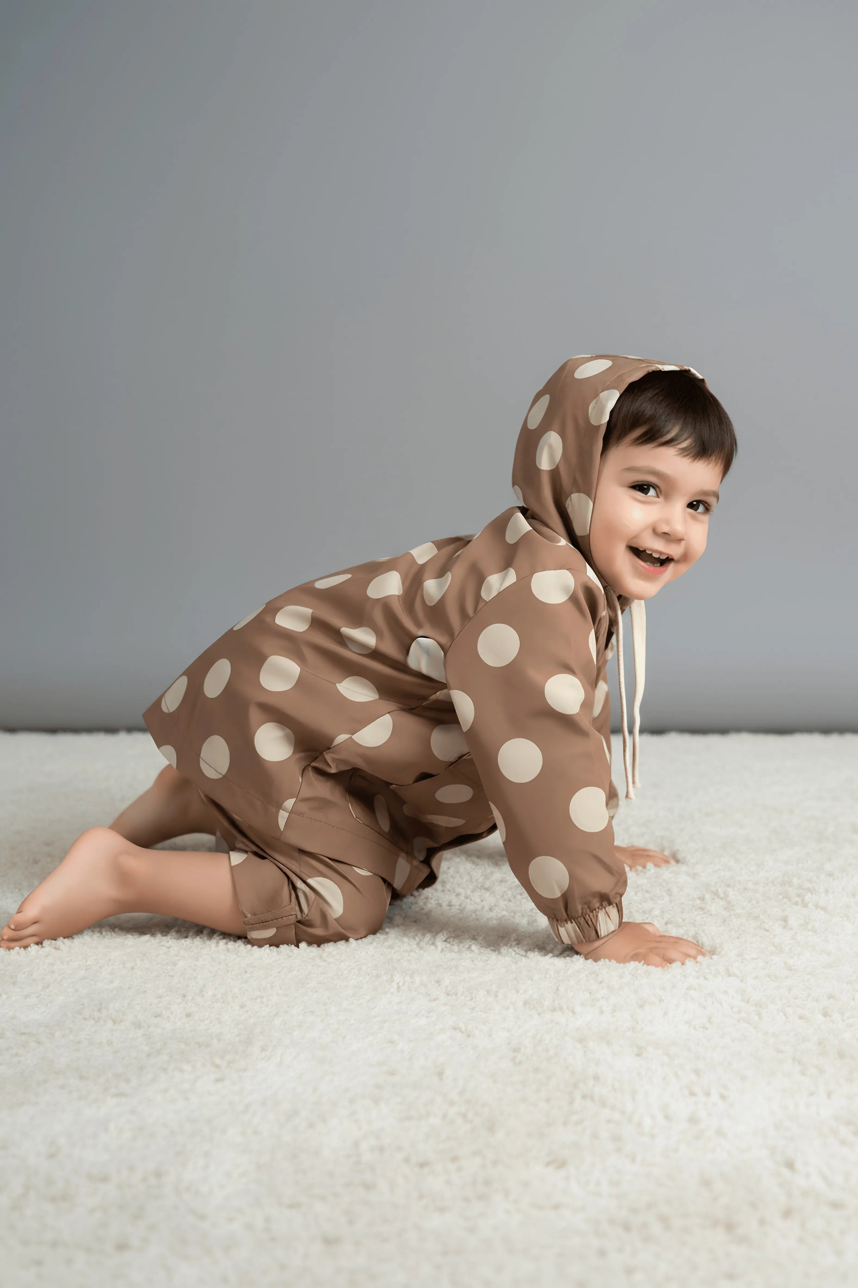 Child wearing a brown polka dot Bubba's and Mama's windbreaker on a light gray background