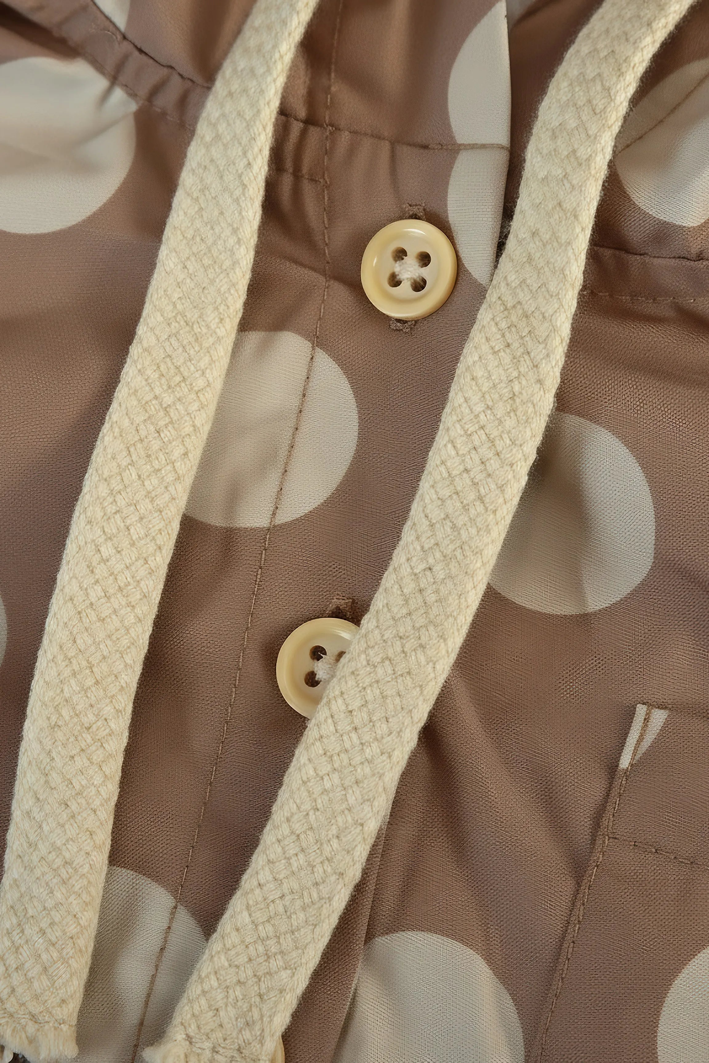 Close-up of a brown fabric with beige polka dots and buttons, featuring a beige woven strap.