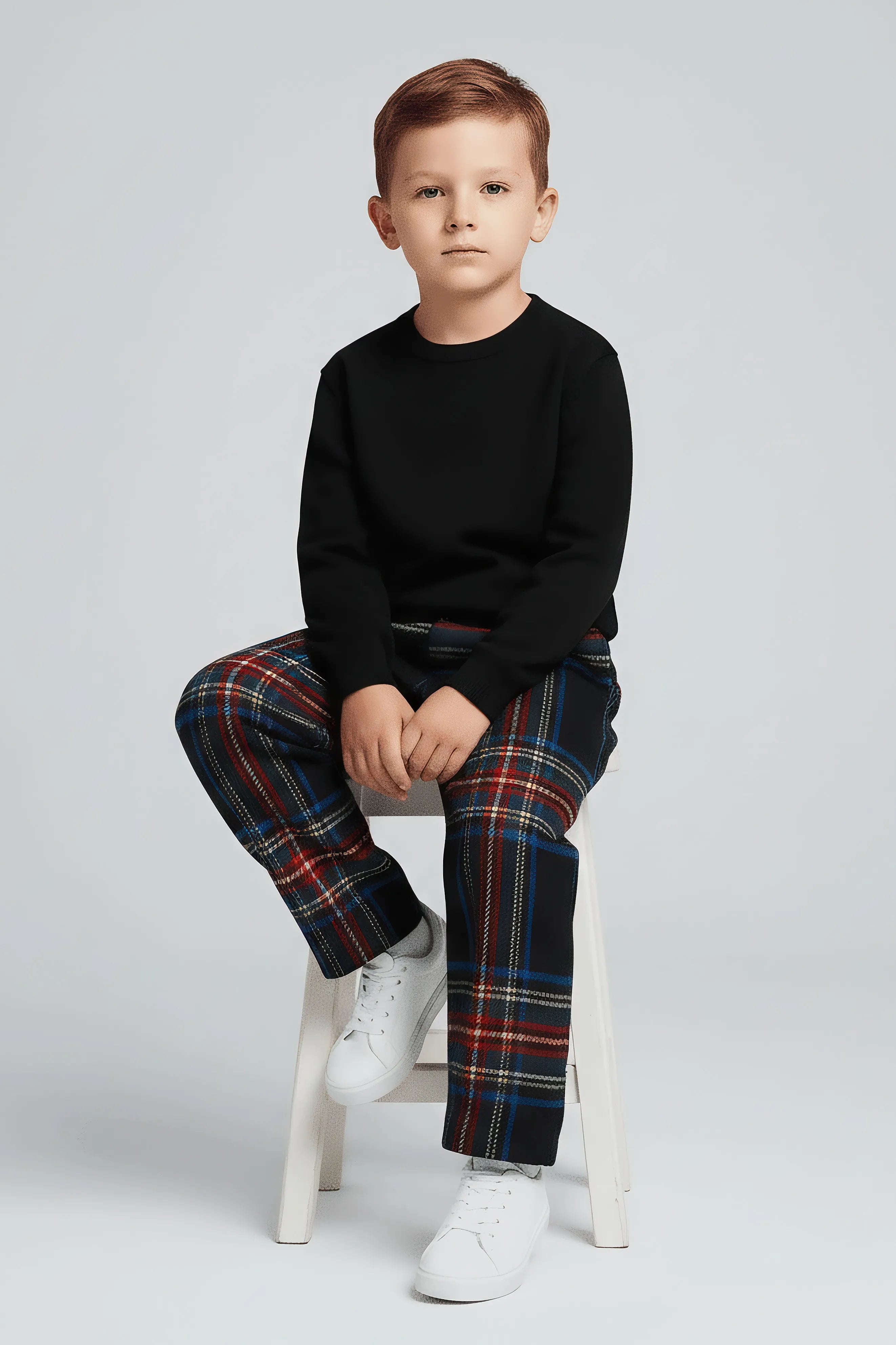 Child wearing a black sweater and plaid Bubba's and Mama's pants sitting on a white stool against a light gray background