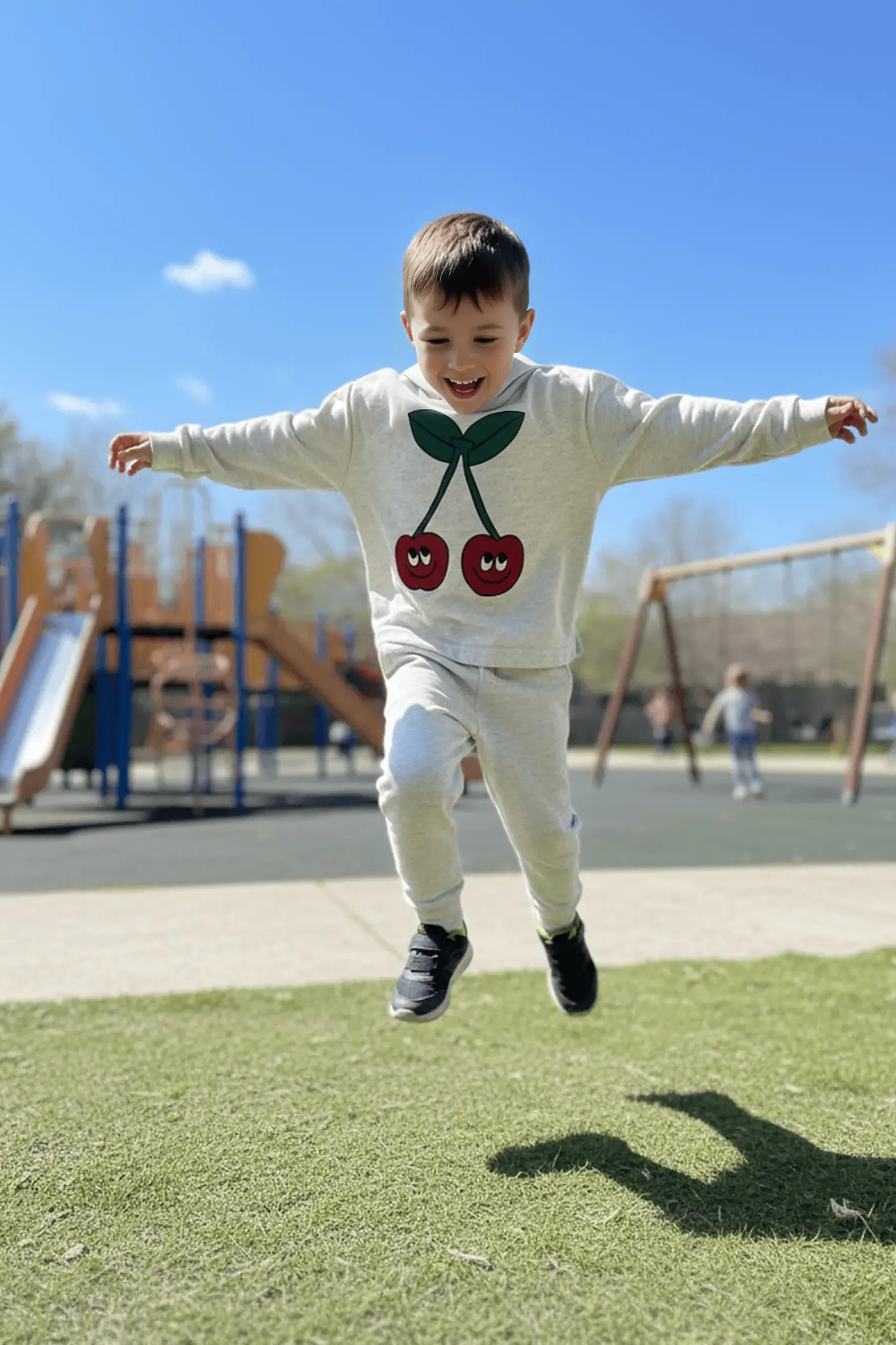 Child jumping in the air on a playground with a clear blue sky.
