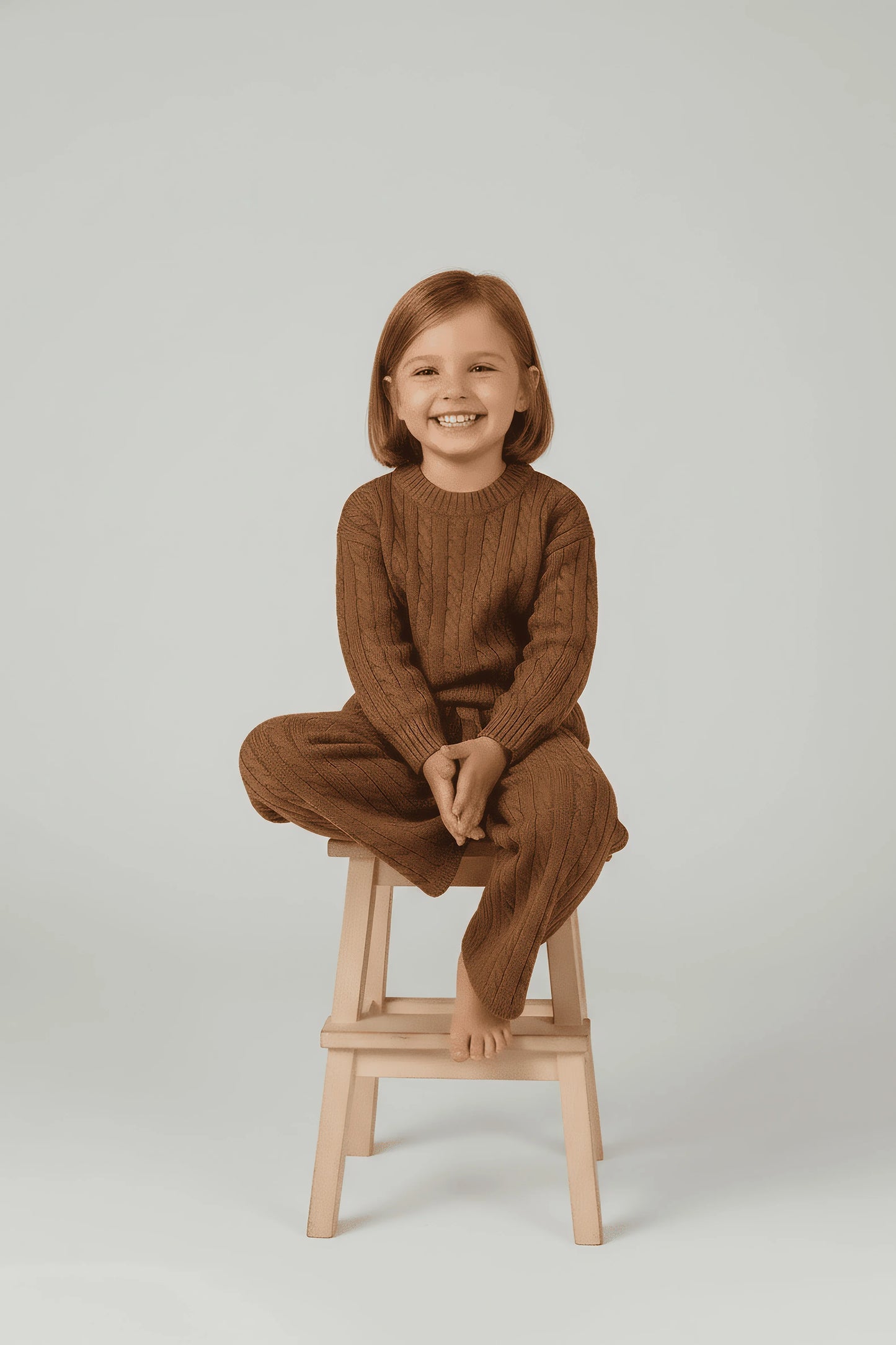 Child wearing a brown Bubba's and Mama's outfit sitting on a wooden stool against a plain background