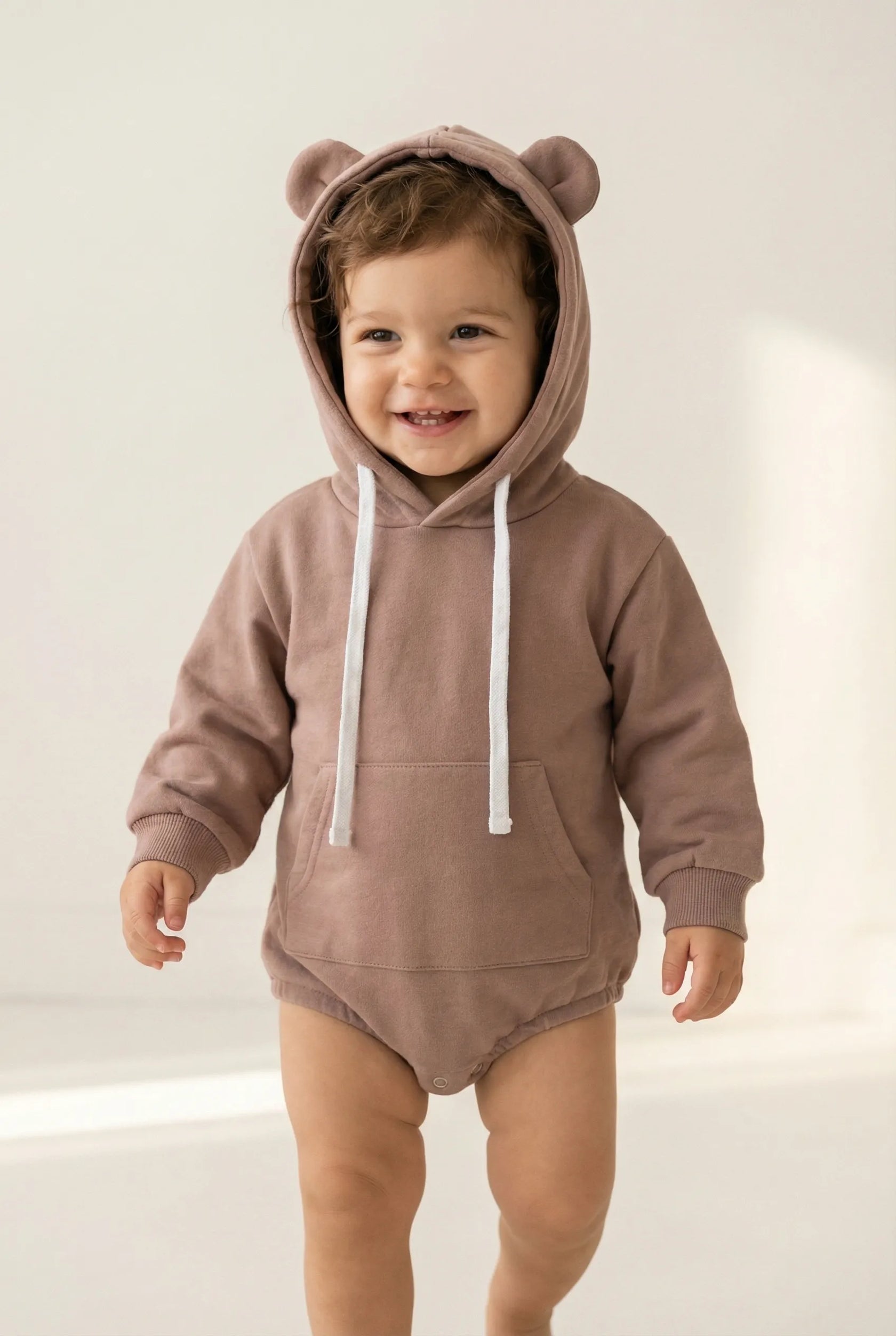 Child wearing a brown bear-themed hoodie and onesie on a light background