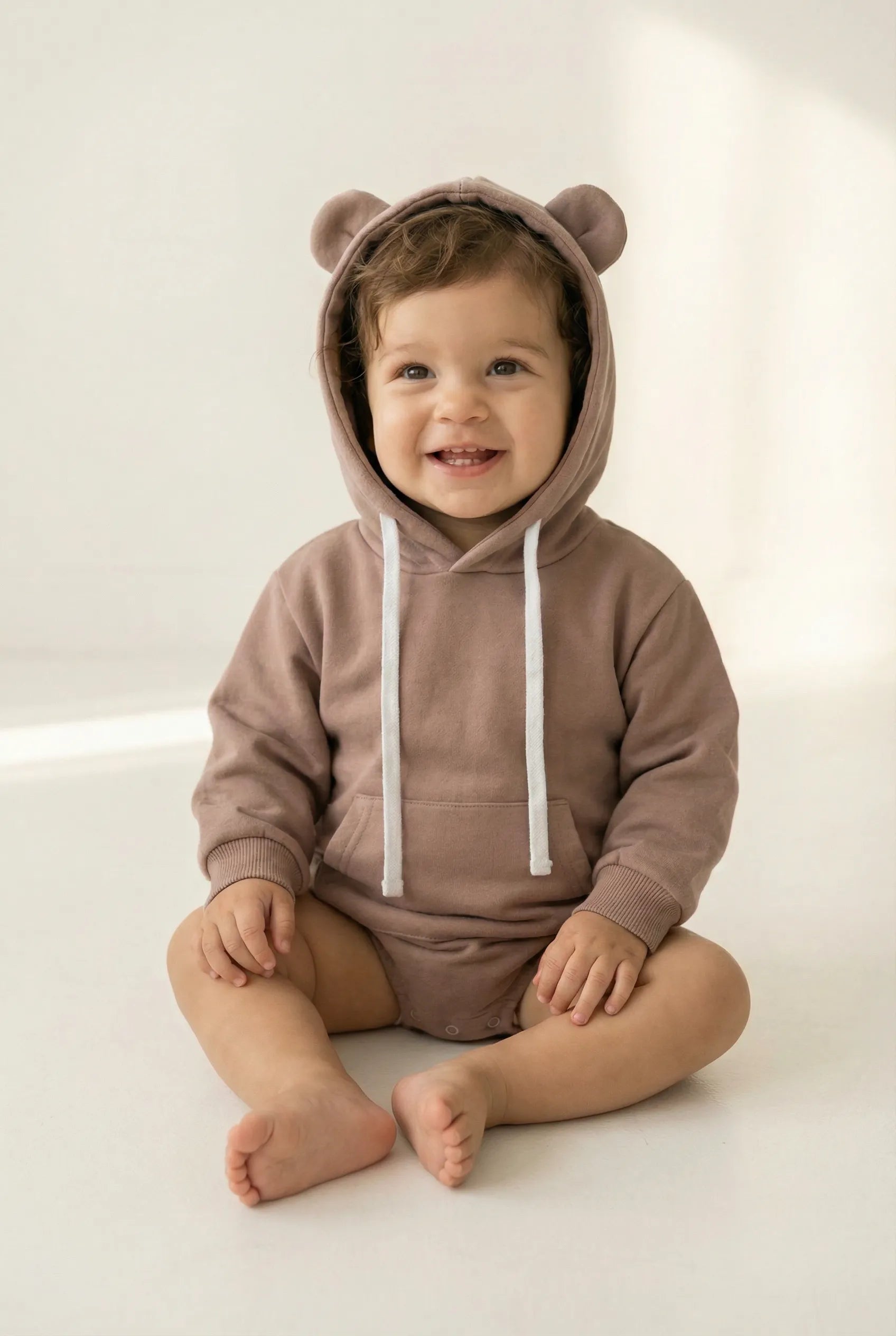 Child wearing a brown bear-themed onesie with a hood on a white background