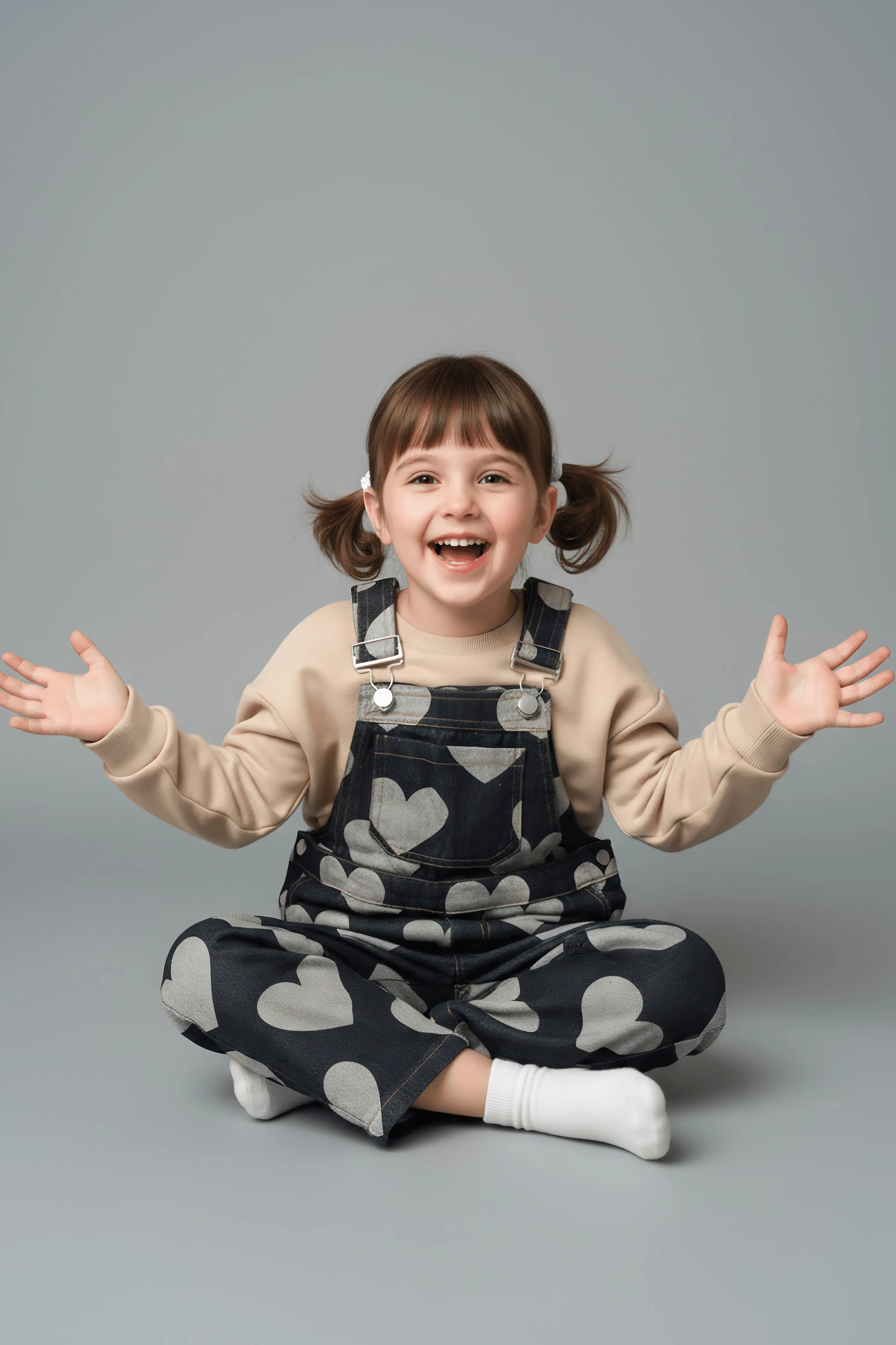 Child wearing a heart-patterned denim Bubba's and Mama's overalls and beige sweater on a gray background