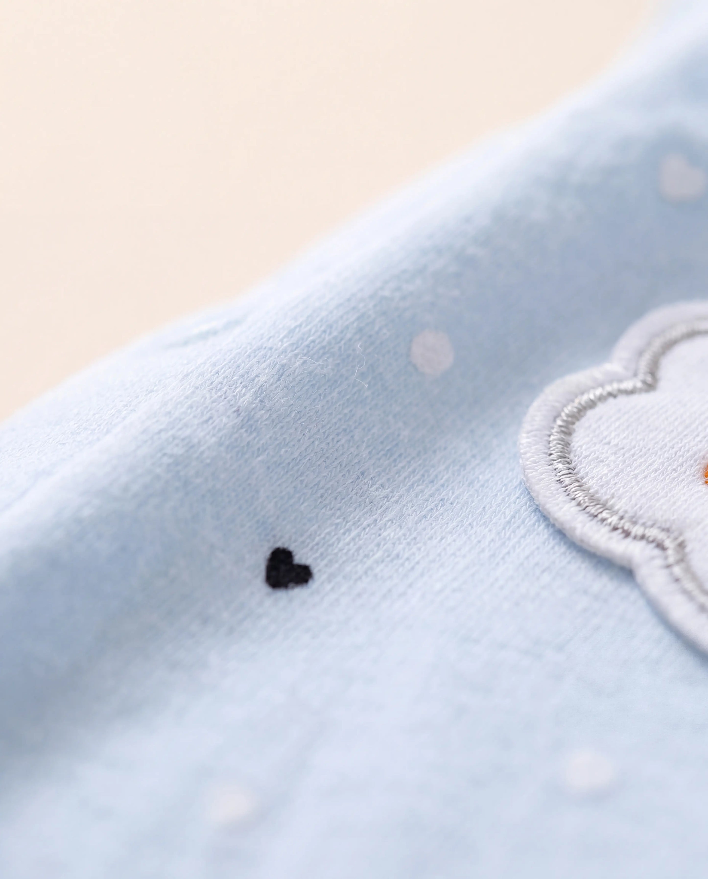 Close-up of a light blue fabric with a cloud design and black heart on a beige background
