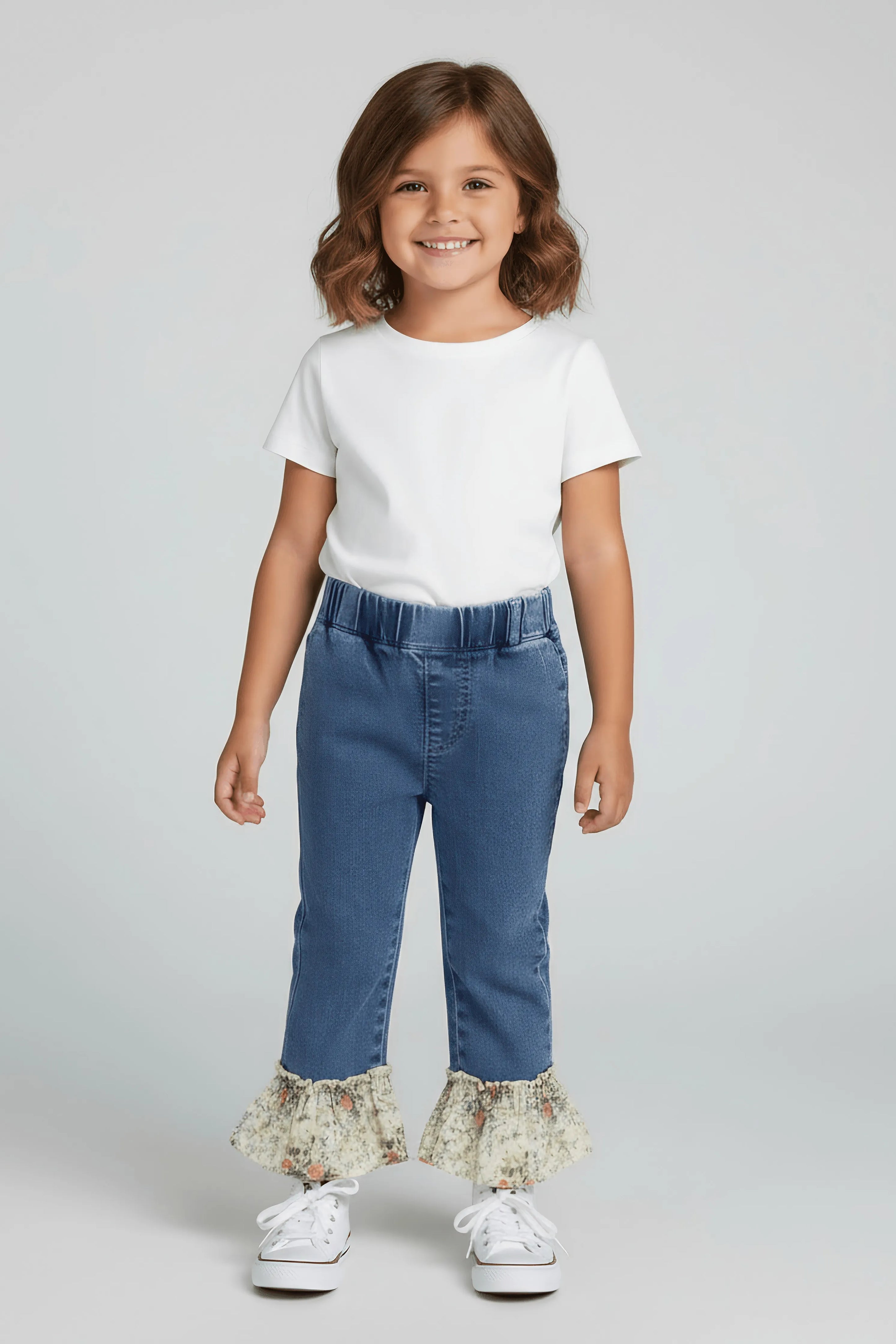 Young girl wearing a white t-shirt and blue jeans with ruffled hem on a light gray background
