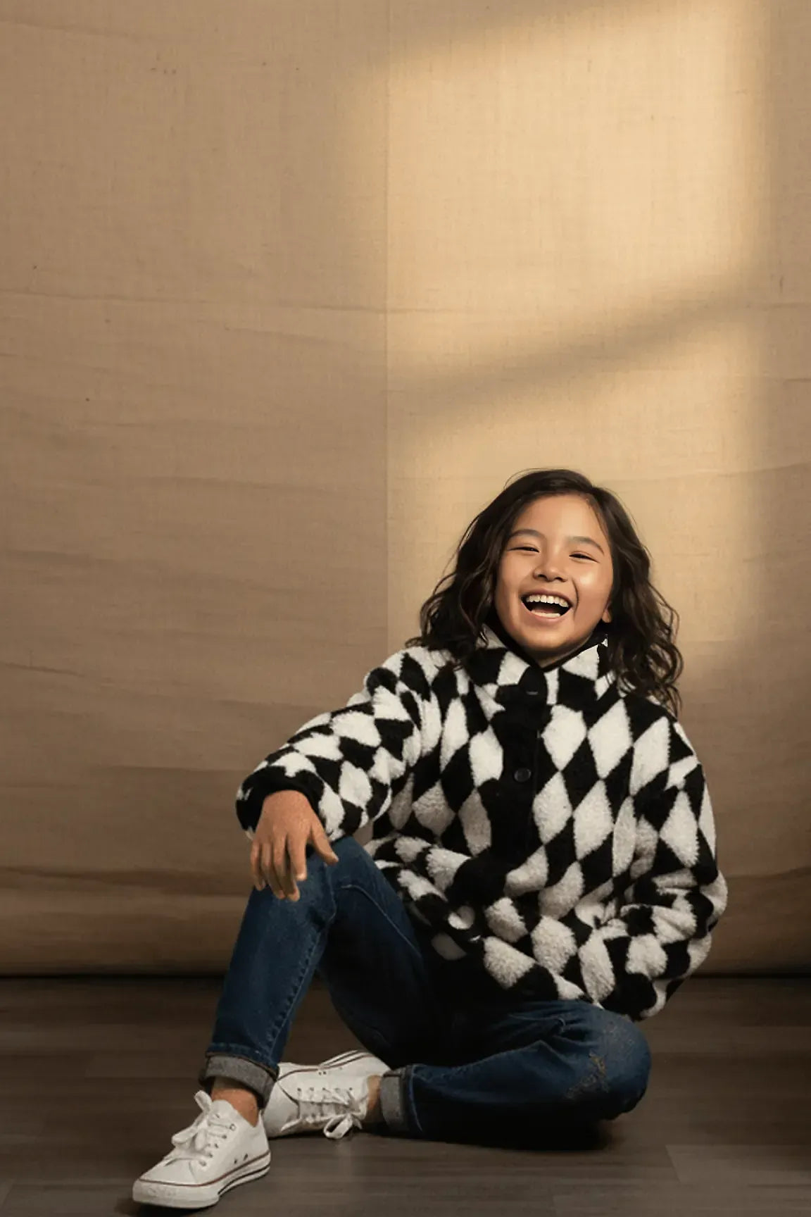 Person wearing a black and white checkered sweater sitting on the floor with a warm light casting shadows.