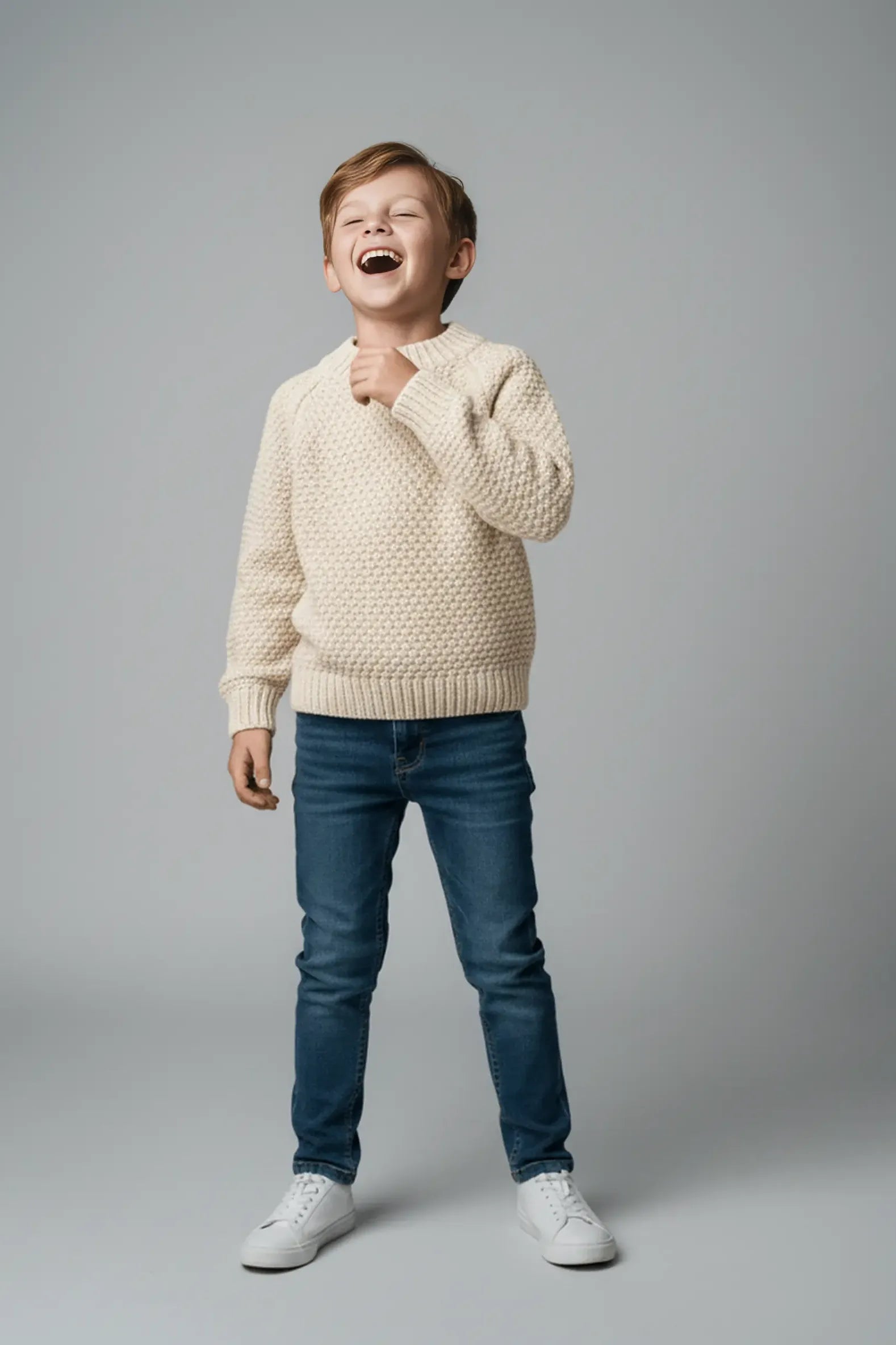 Child wearing a cream Bubba's and Mama's sweater and blue jeans on a gray background