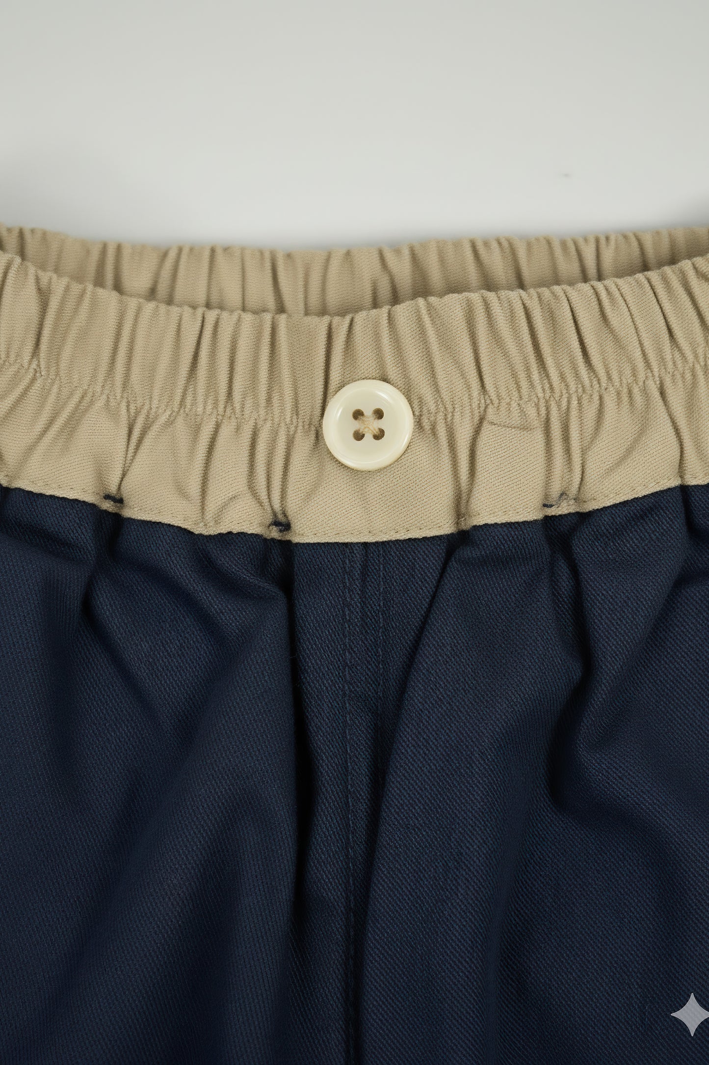 Navy shorts with beige waistband and button on a white background