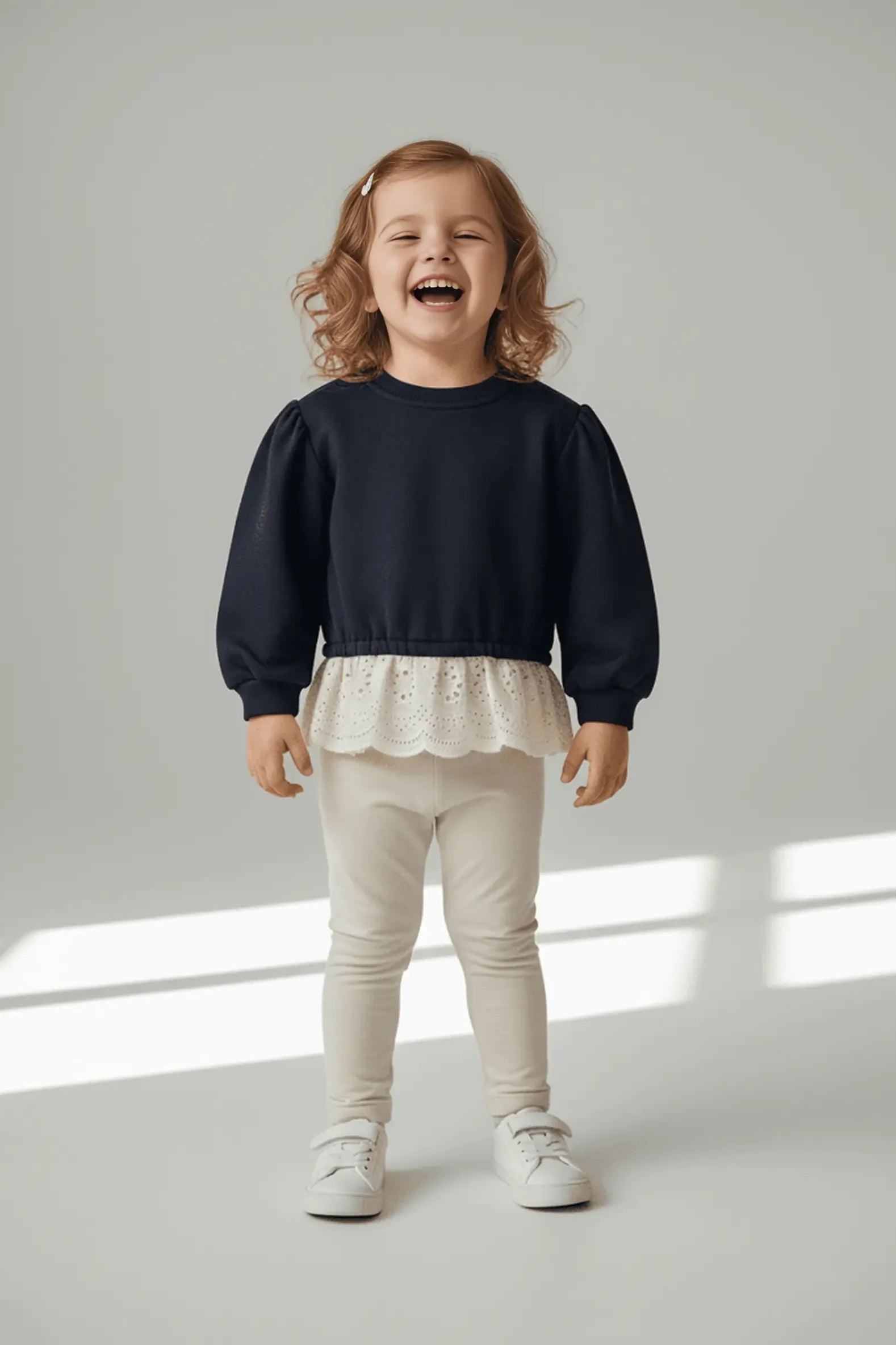 Child wearing a navy blue Bubba's and Mama's top with a white lace trim and beige pants on a light gray background