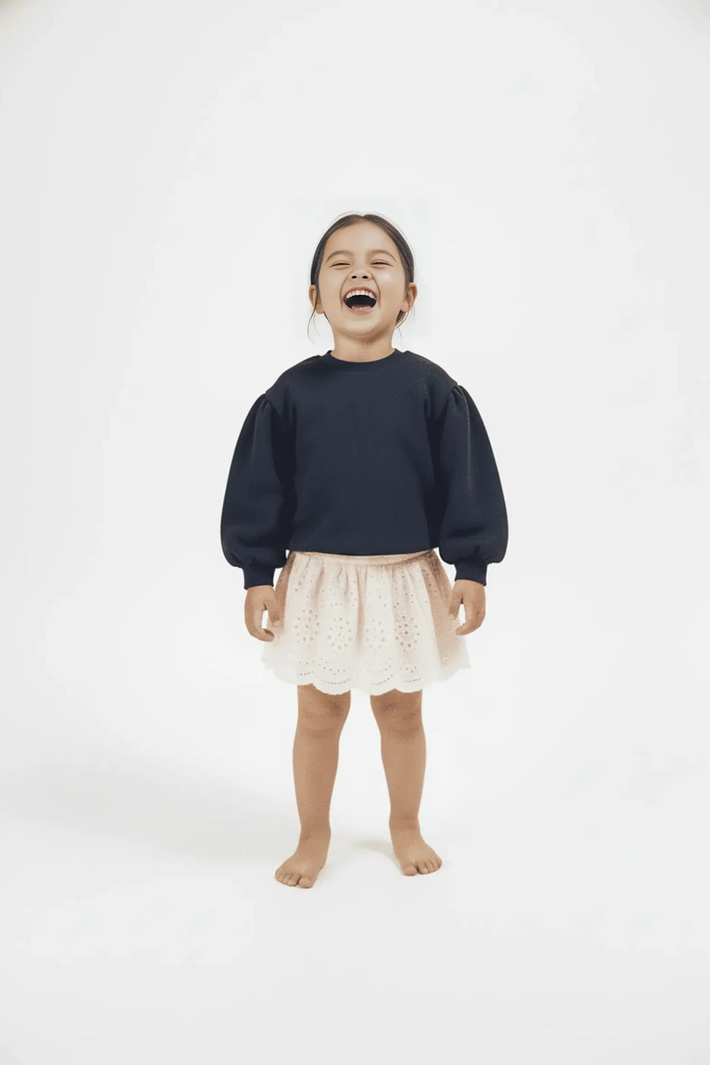 Child wearing a navy Bubba's and Mama's sweater and white skirt on a white background