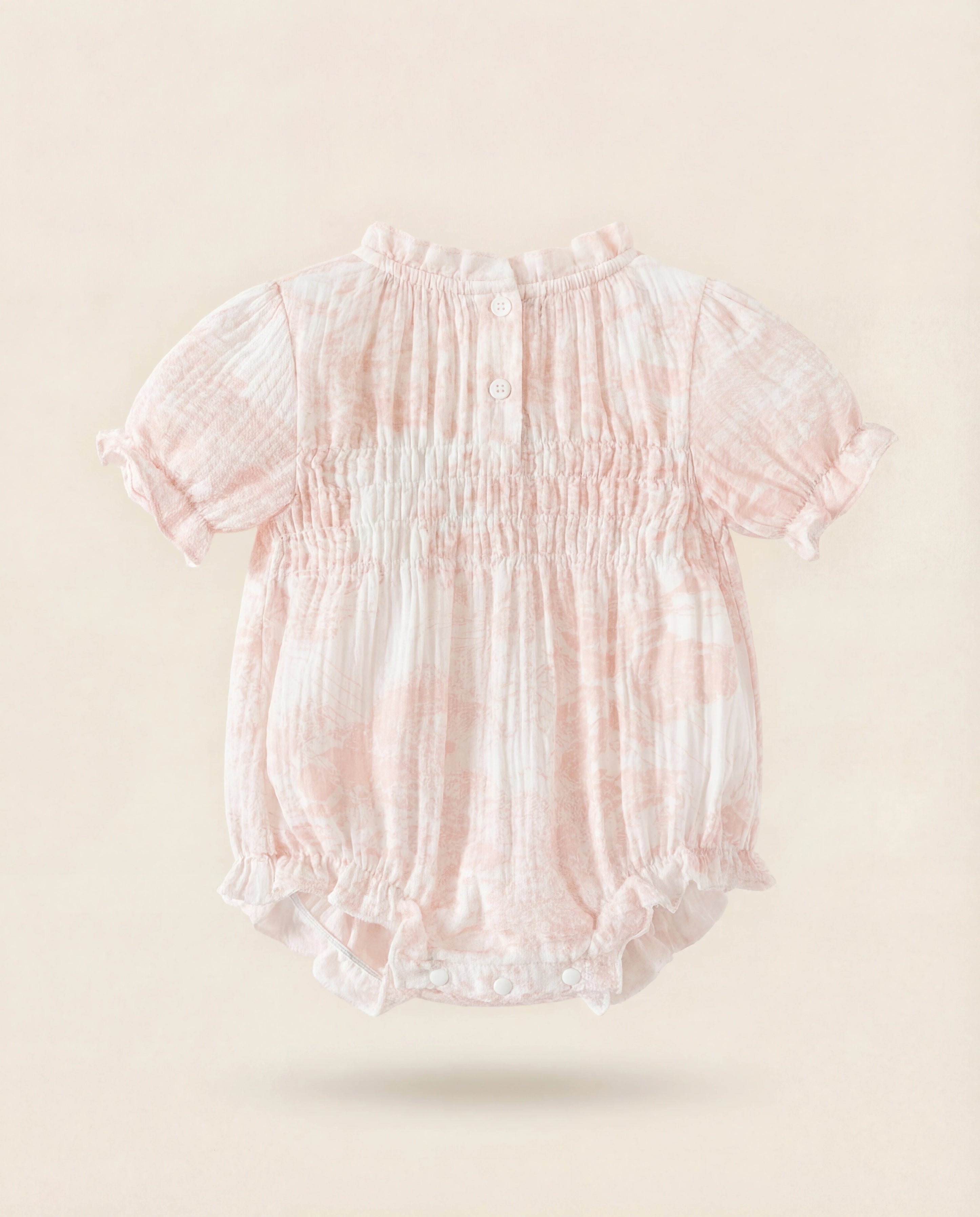 Pink baby romper with ruffled details on a beige background