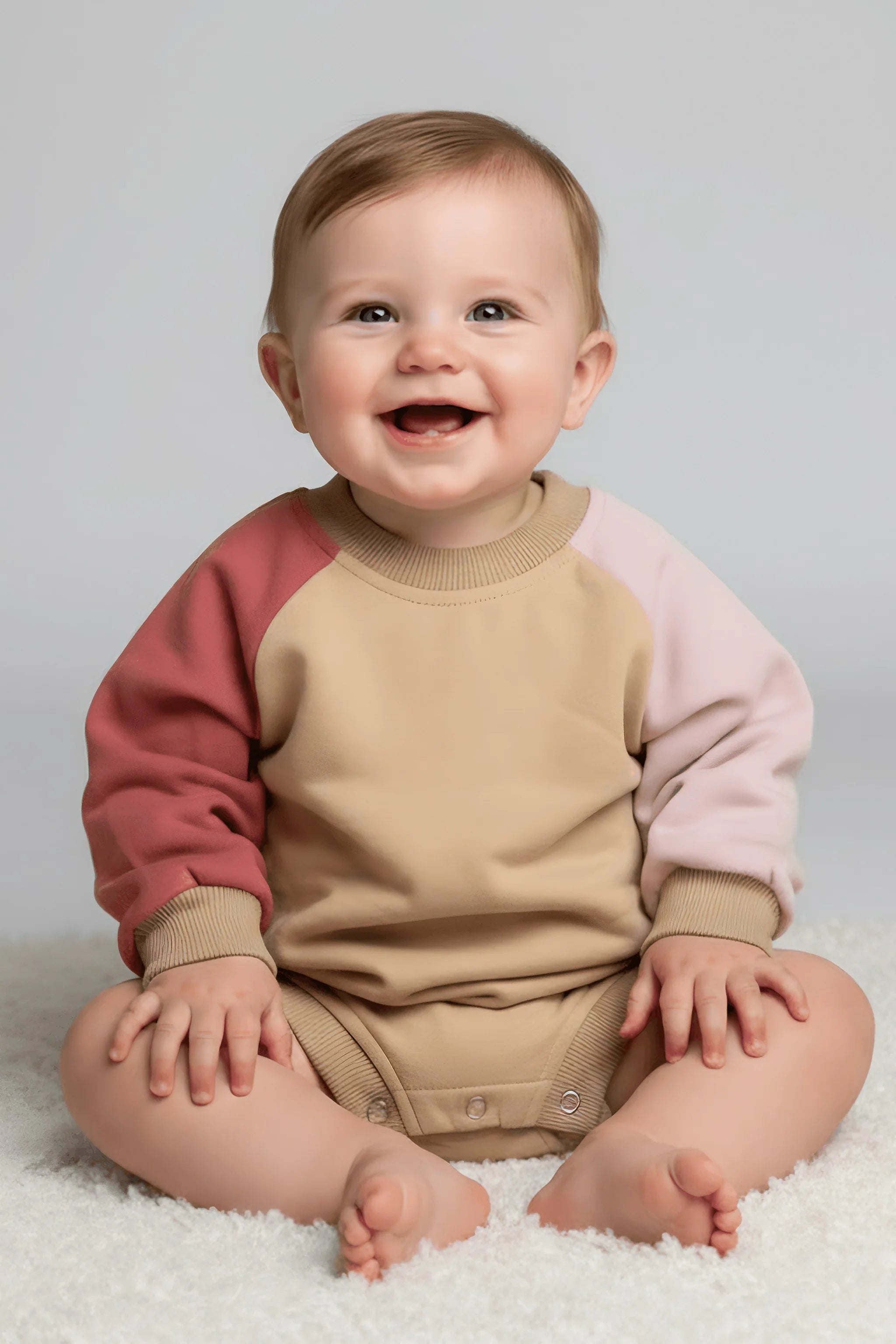 Baby wearing a two-tone pink and beige sweater sitting on a white surface.