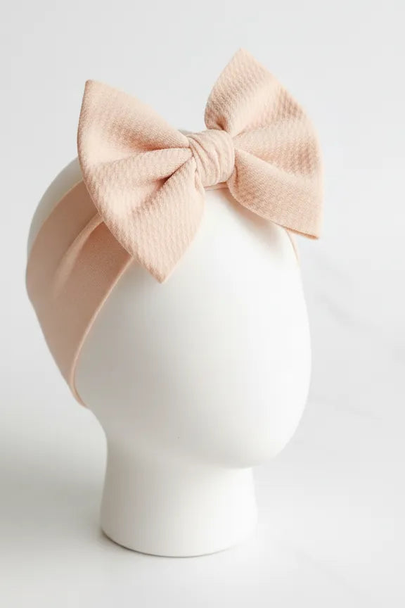Blush pink headband with bow on a mannequin head against a white background