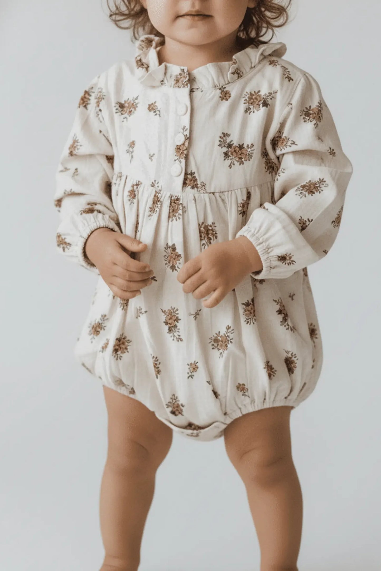Child wearing a floral Bubba's and Mama's romper against a plain background