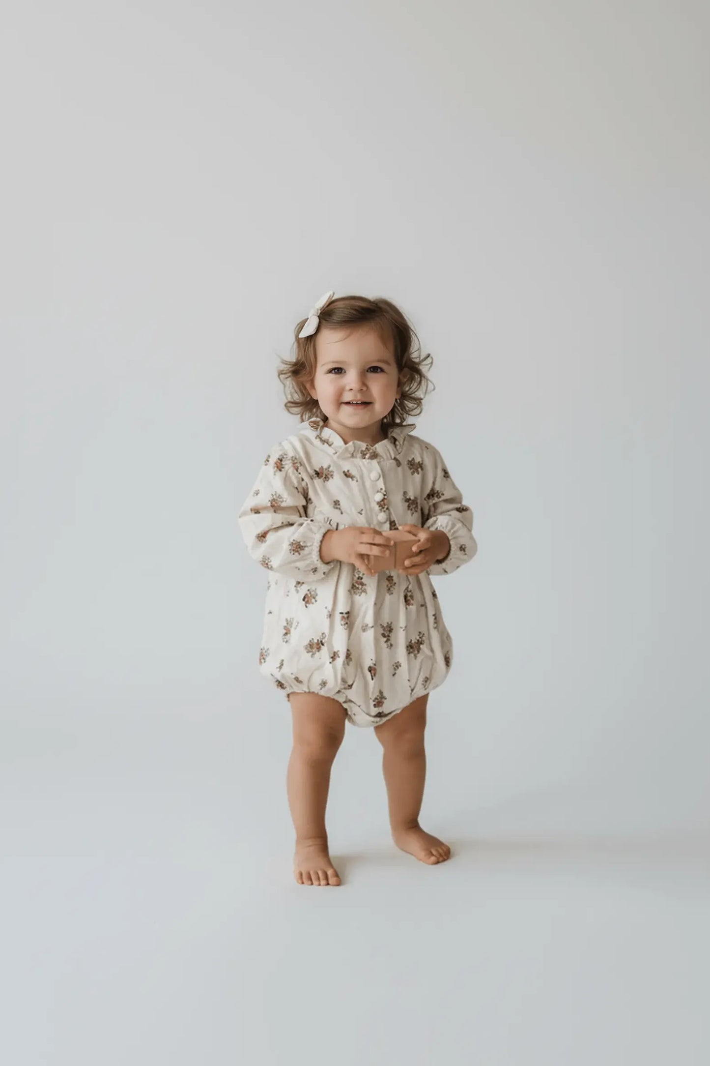 Child wearing a floral Bubba's and Mama's onesie on a plain background