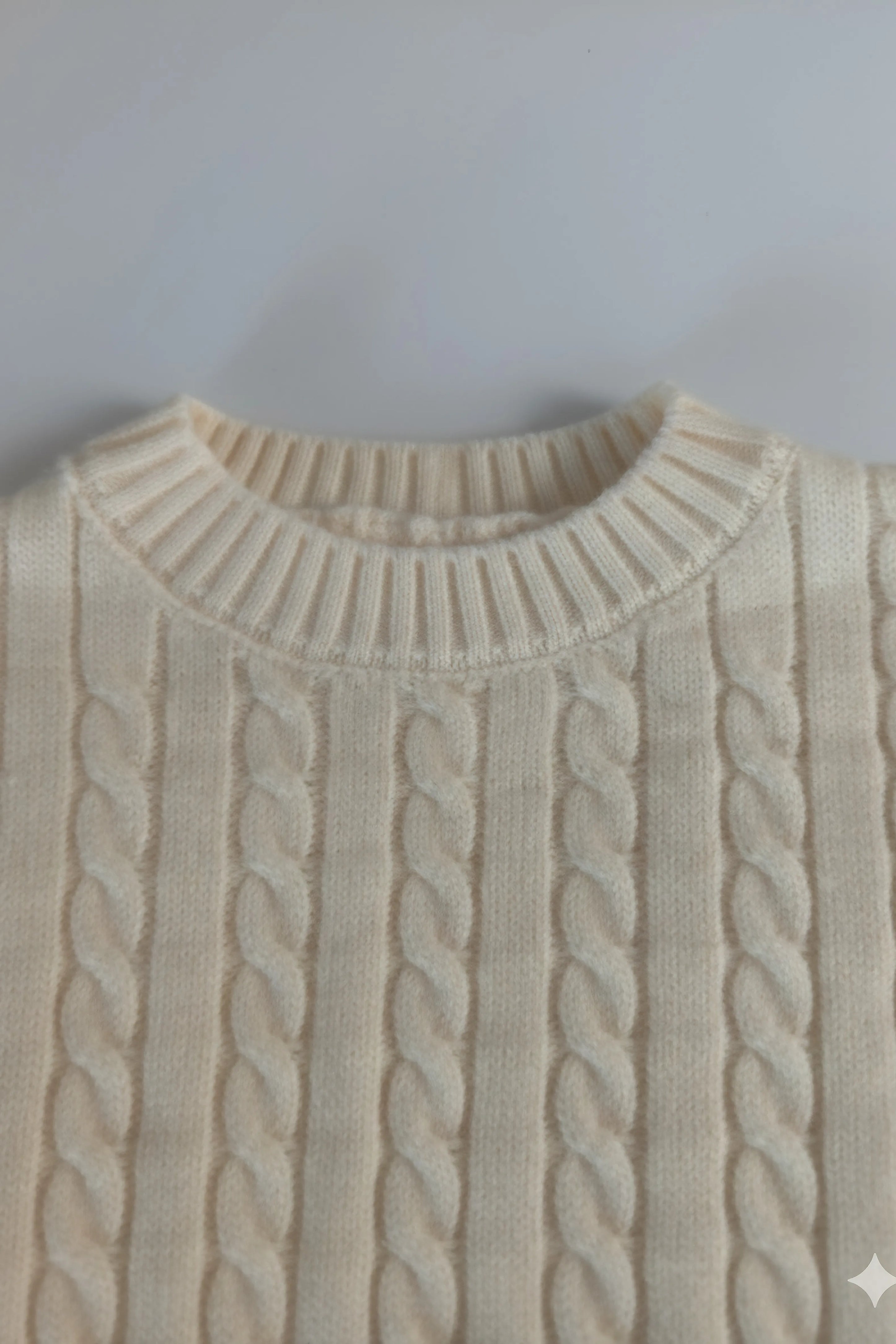 Close-up of a beige cable knit Bubba's and Mama's sweater on a light gray background