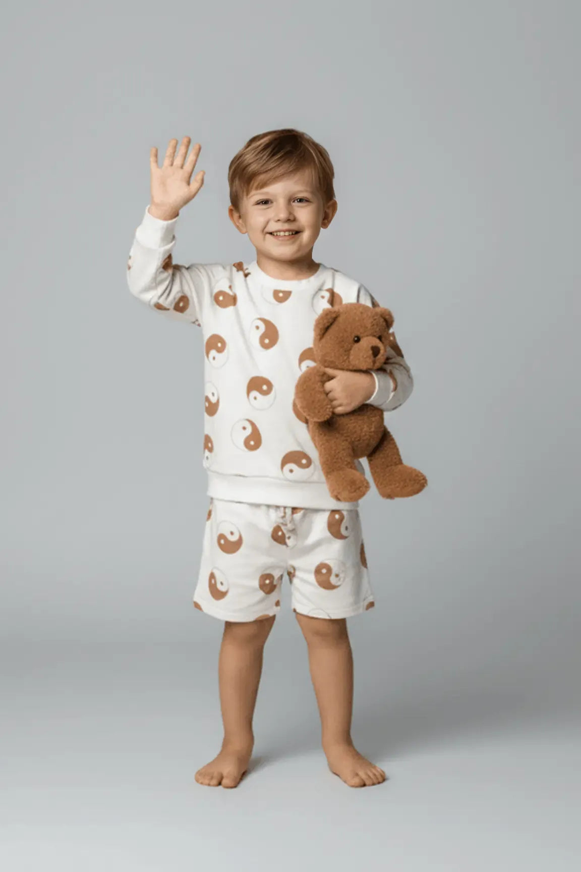 Child wearing a Bubba's and Mama's pajama set with bear pattern holding a teddy bear on a gray background