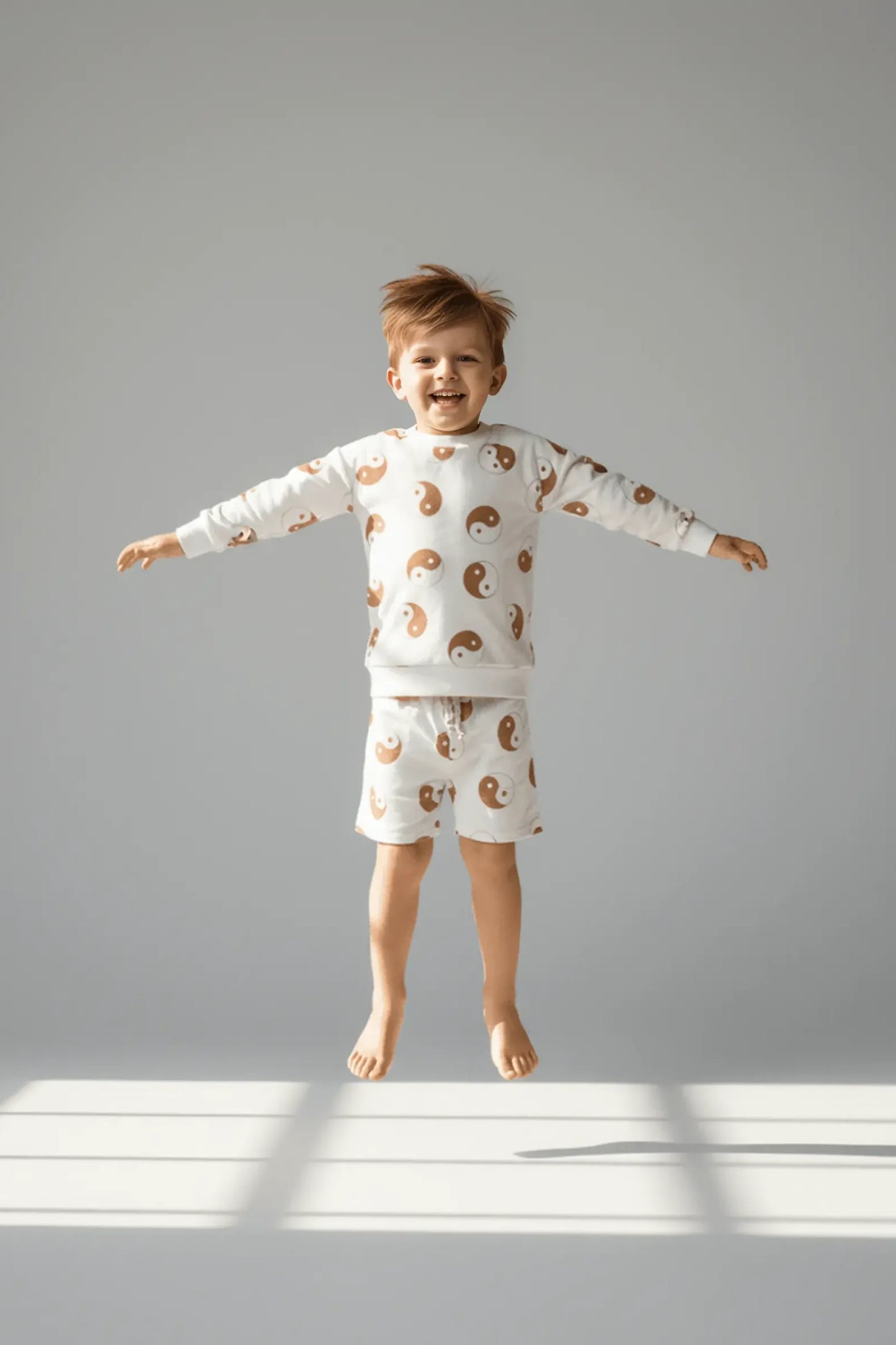 Child wearing a patterned Bubba's and Mama's pajama set standing on a light gray floor with a white wall background